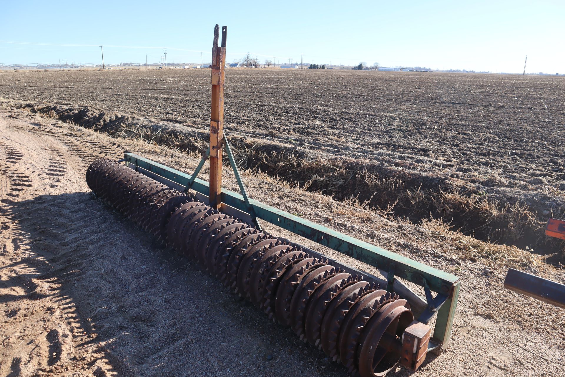 A rusty roller is sitting in the middle of a dirt field