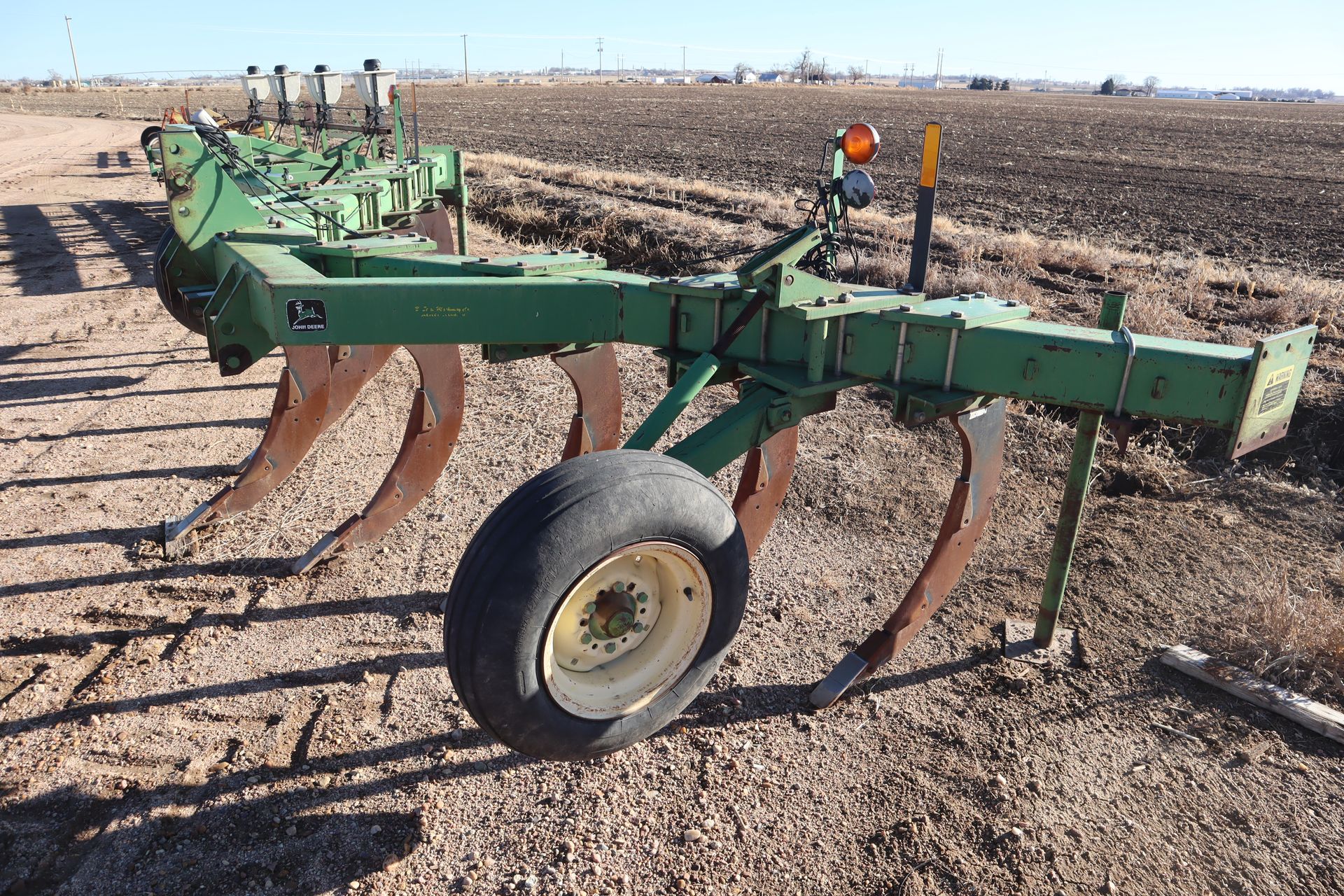 A green plow is sitting in the middle of a dirt field.