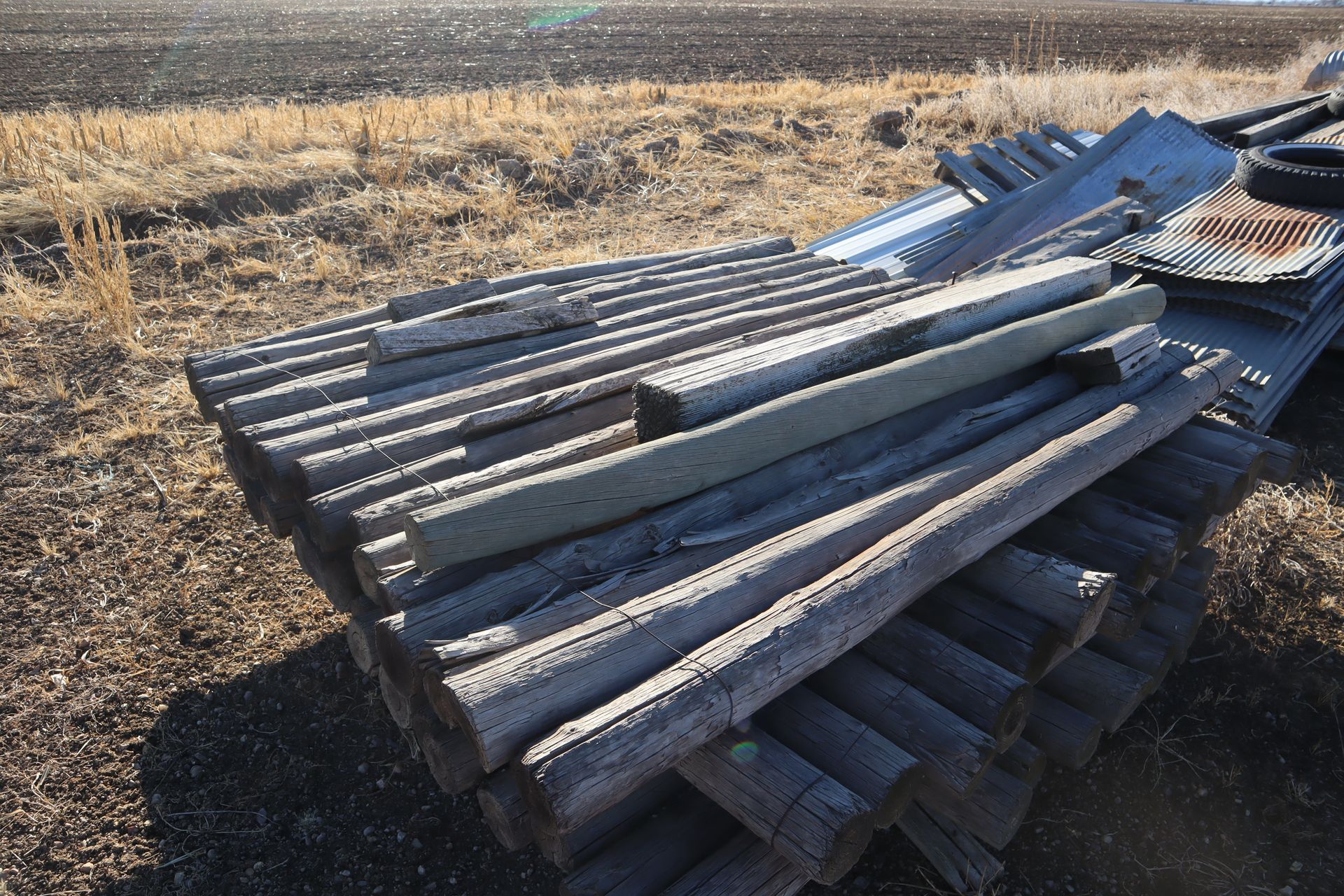 A pile of wooden poles are stacked on top of each other in a field