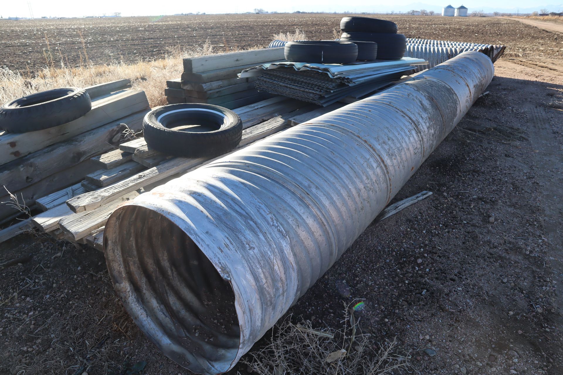 A large metal pipe is laying on the ground next to a pile of tires