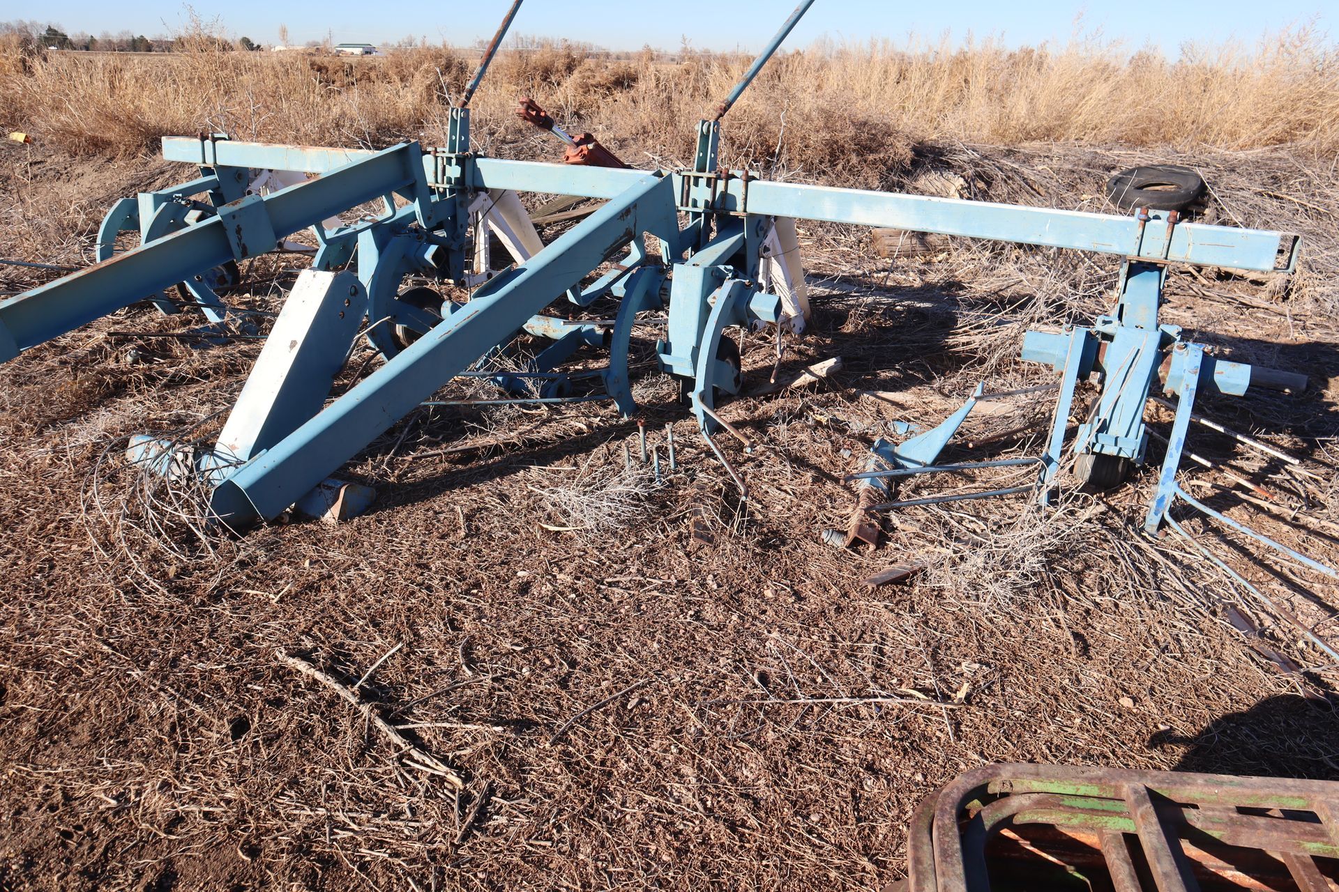 A blue plow is sitting in the middle of a field