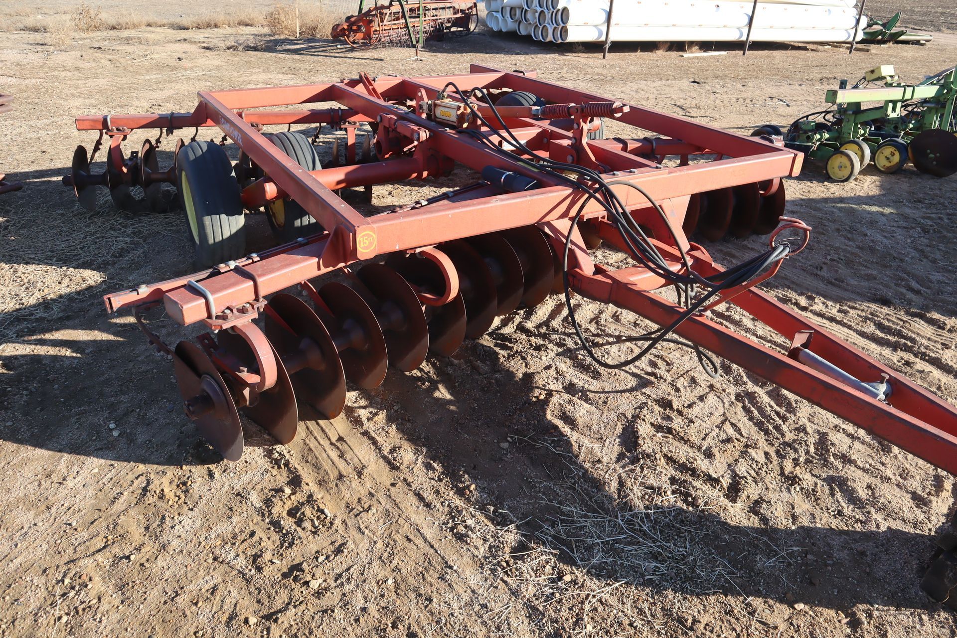 A red tractor is parked in the dirt next to a john deere tractor