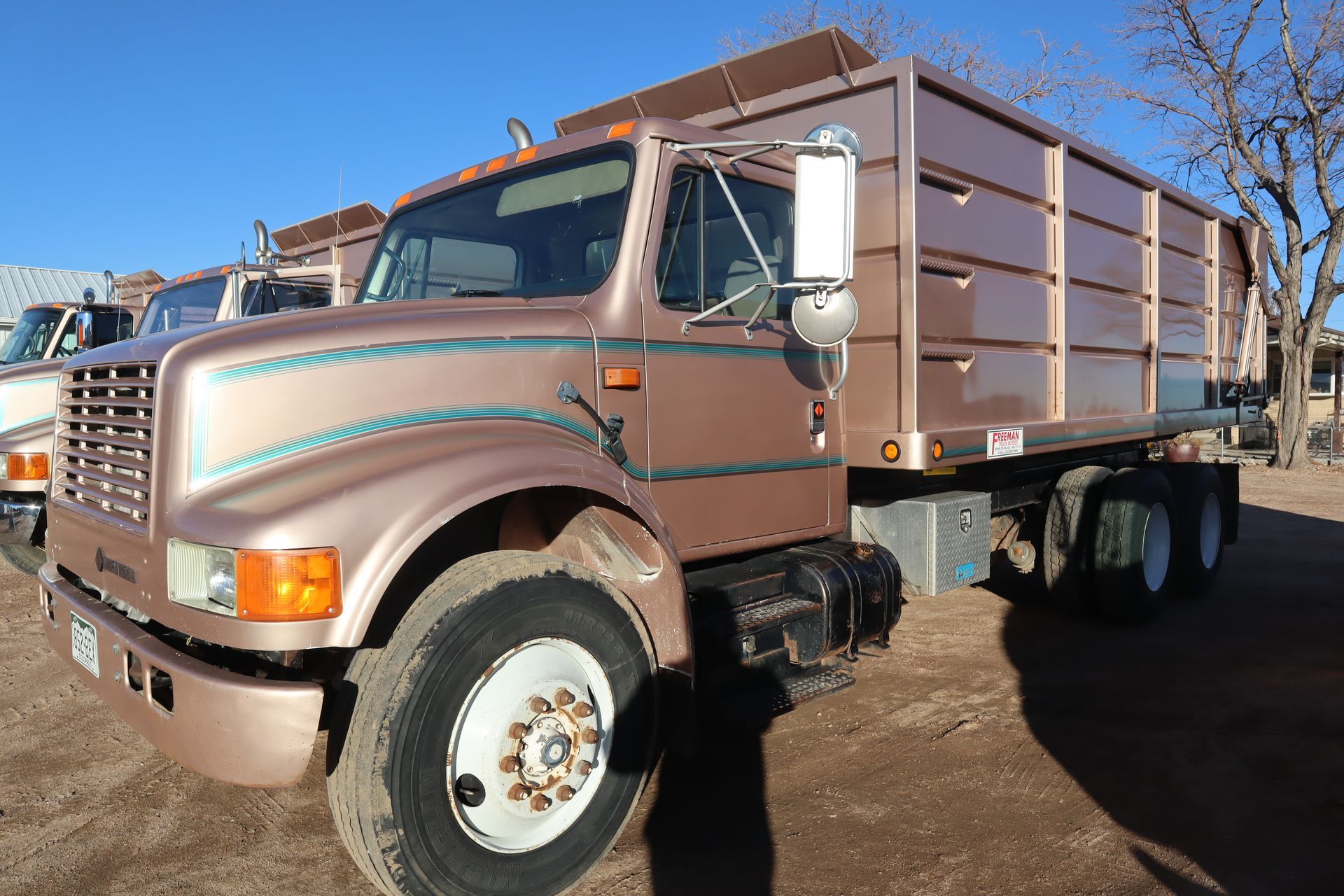 A brown truck with a wooden bed is parked in a dirt field.