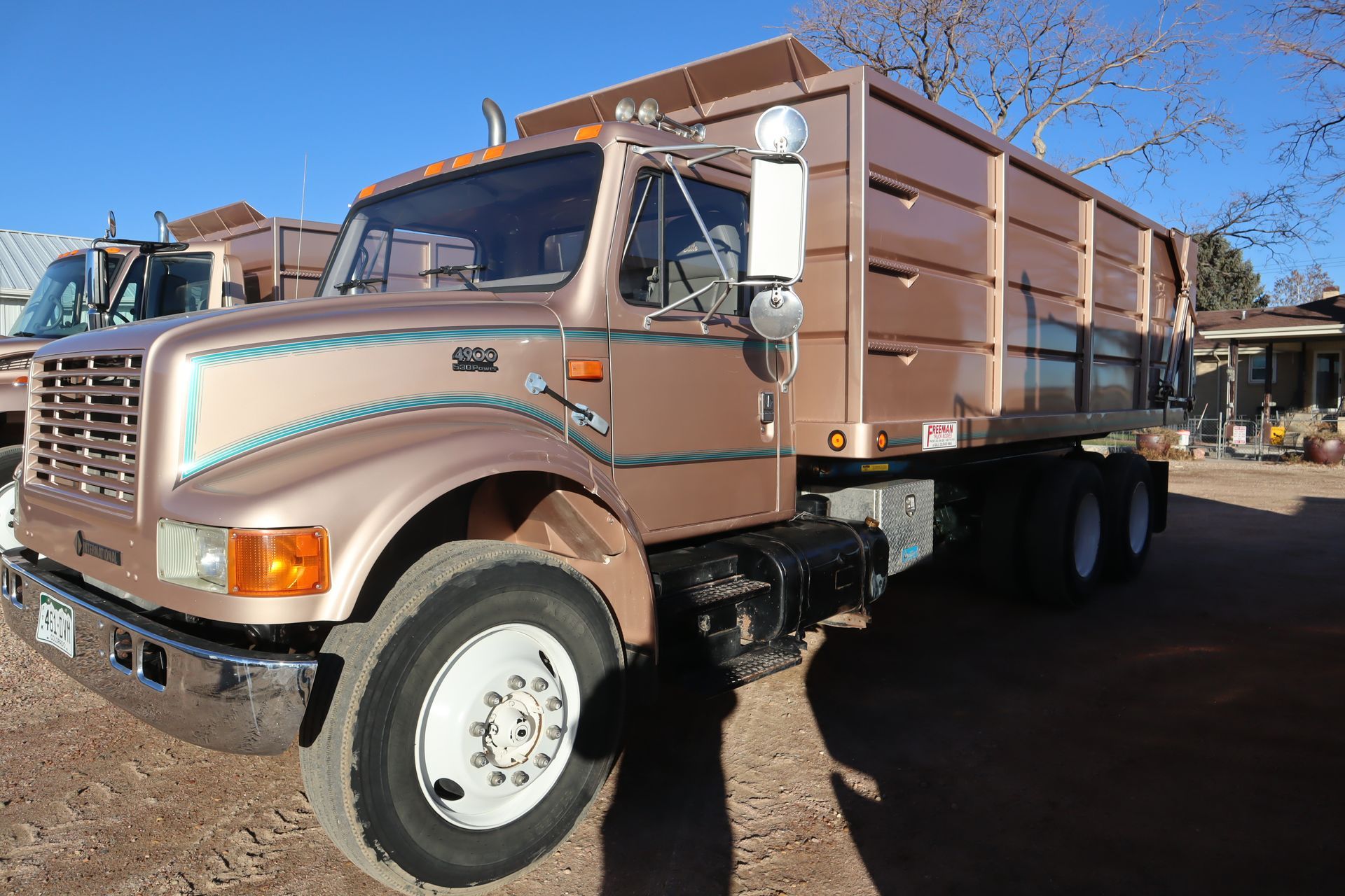 A dump truck is parked in a dirt lot in front of a house.