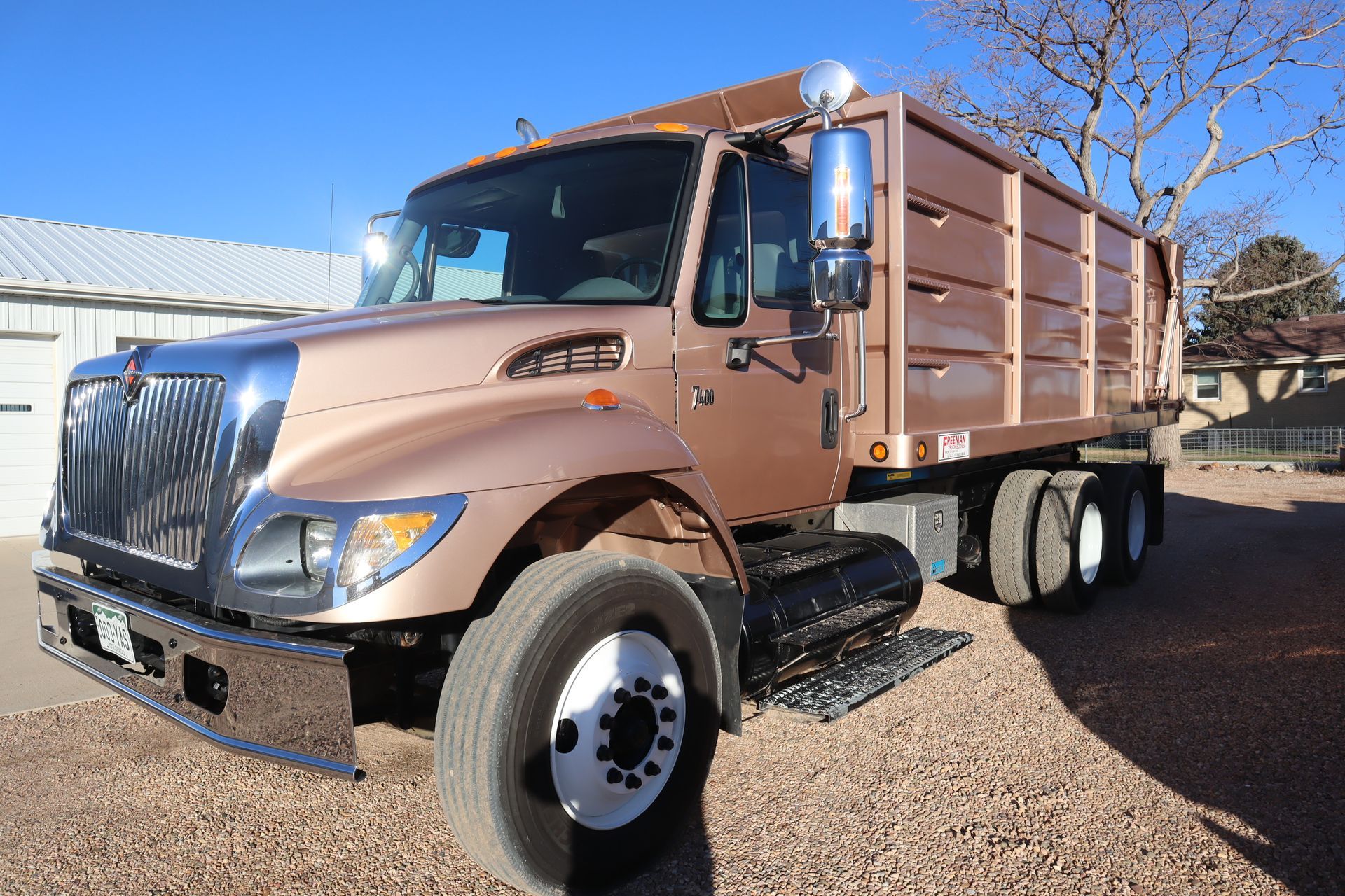 A brown dump truck is parked on a gravel road.