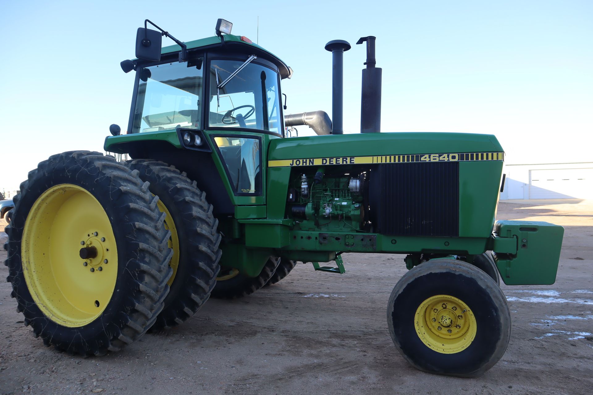A green john deere tractor is parked in a dirt field