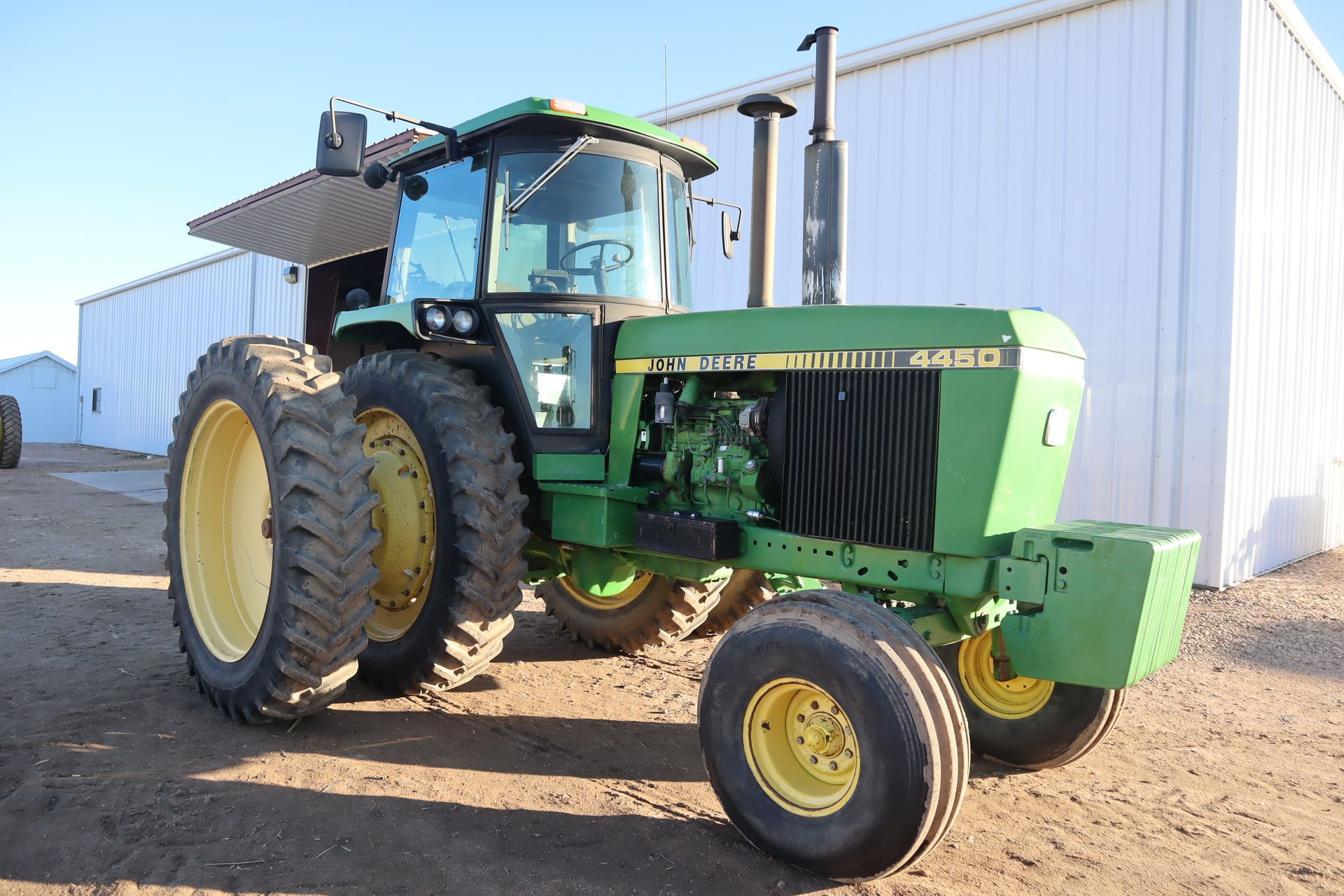 A green john deere tractor is parked in front of a white building