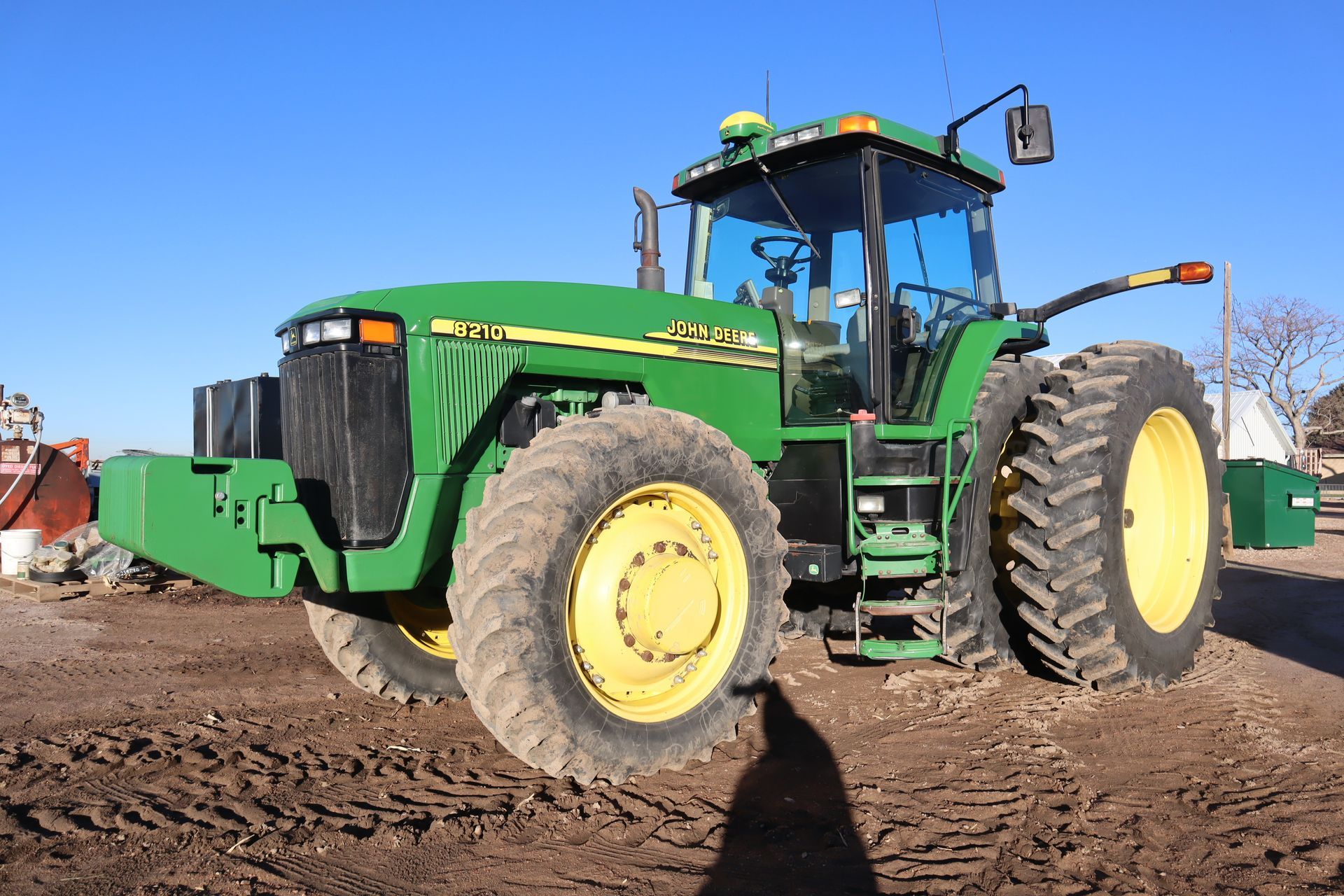 A green and yellow john deere tractor is parked in a dirt field.