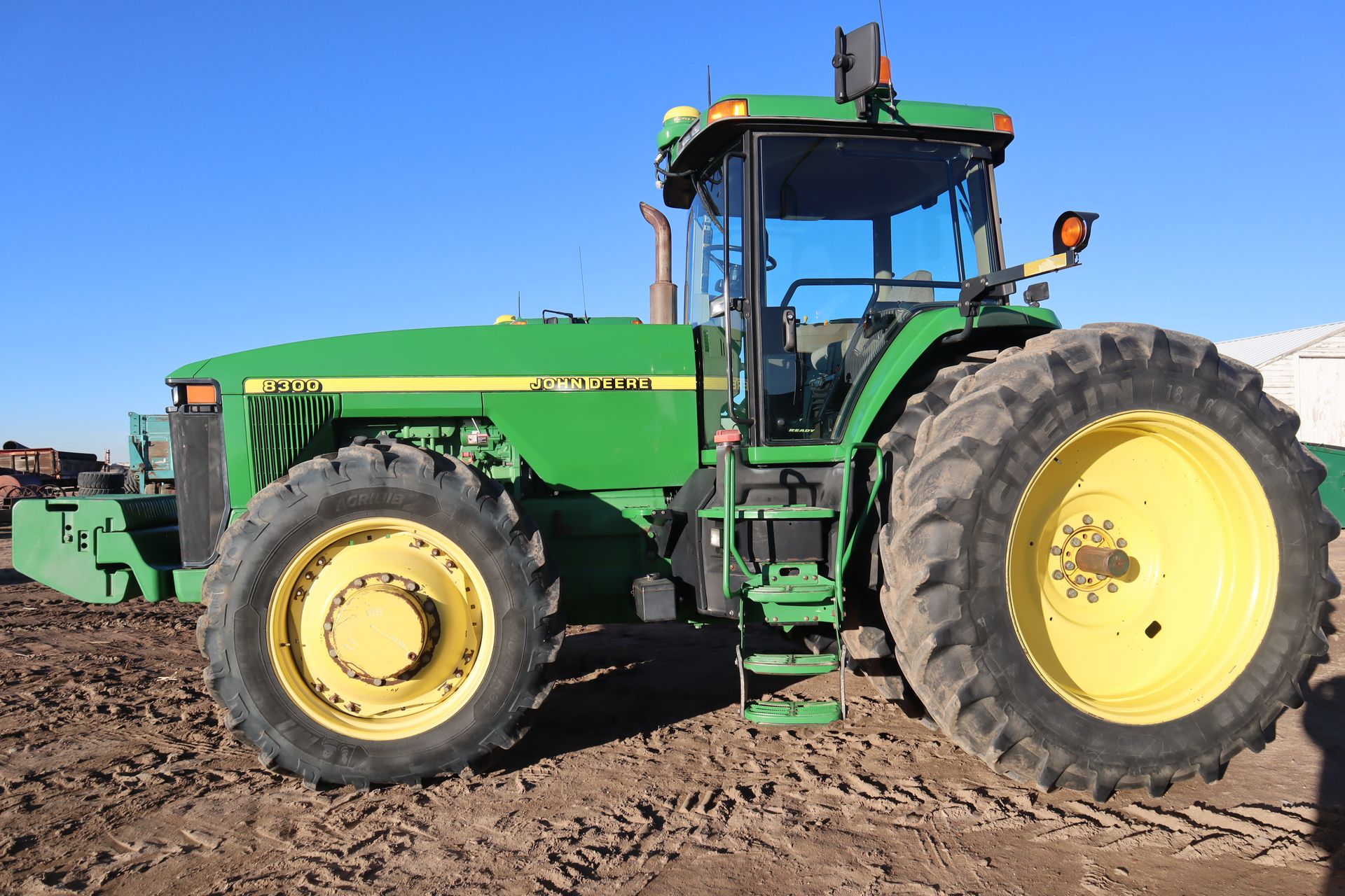 A green john deere tractor is parked in a dirt field