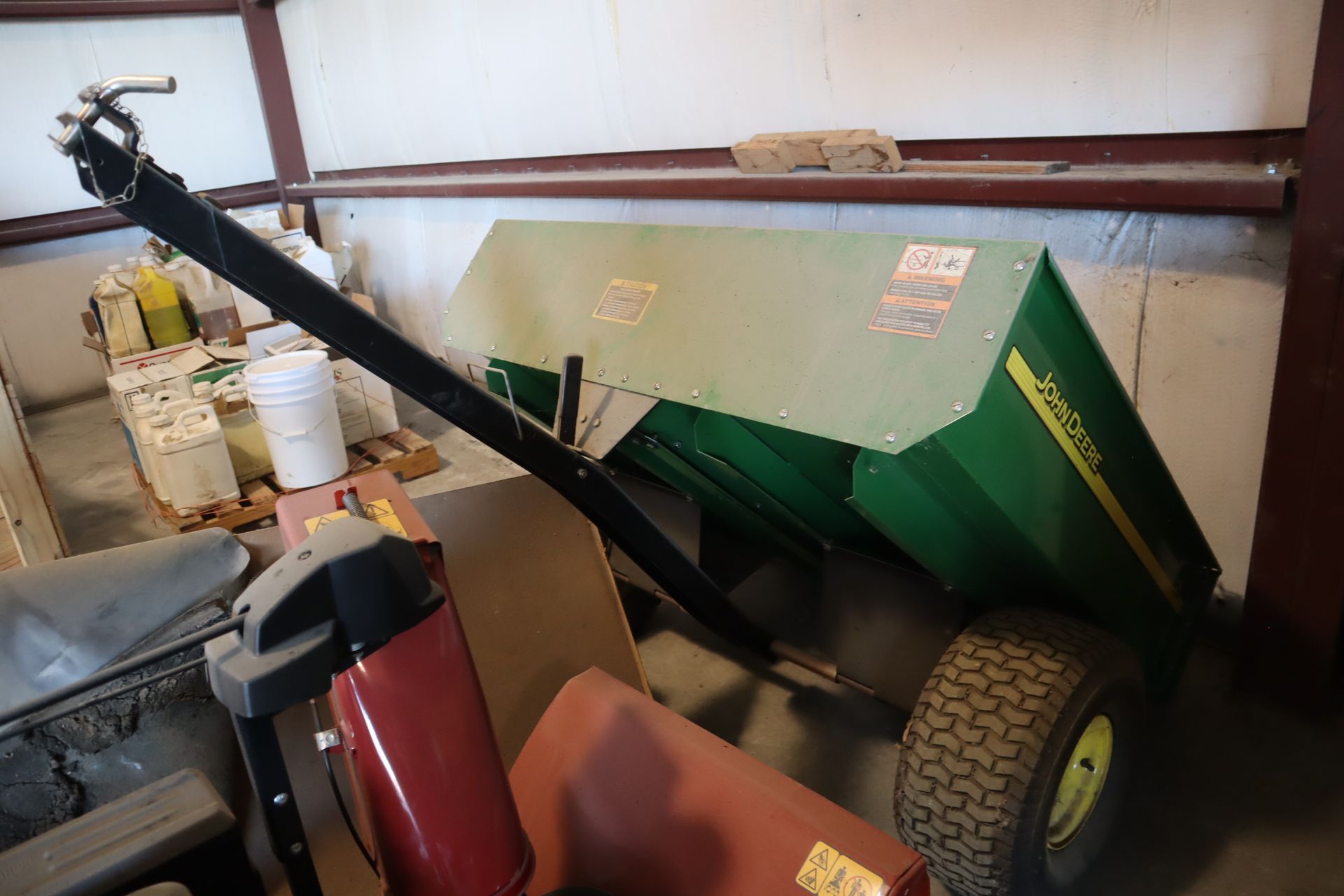 A green john deere trailer is parked in a garage.