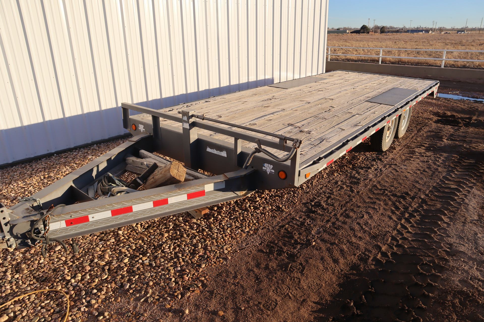 A trailer is parked in the dirt in front of a building.