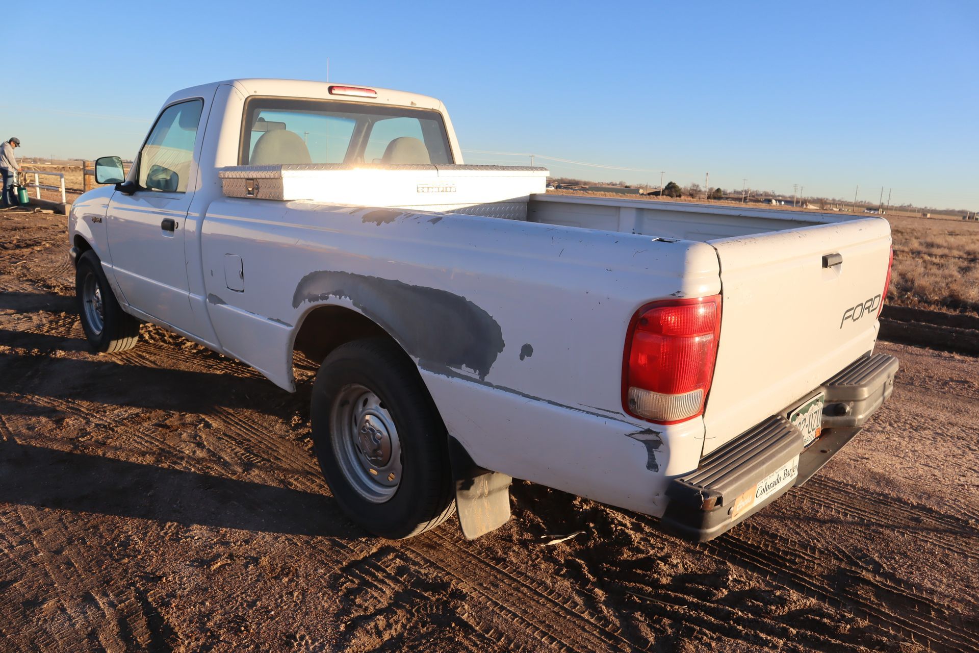 A white pickup truck is parked in the dirt on a dirt road.
