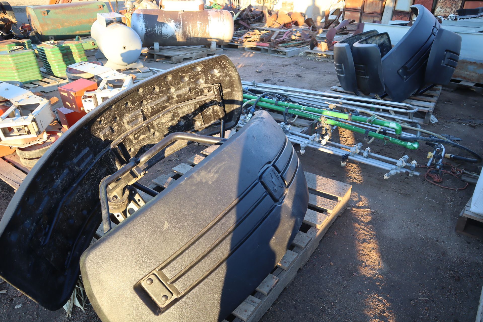A black bumper is sitting on a wooden pallet in a scrap yard.