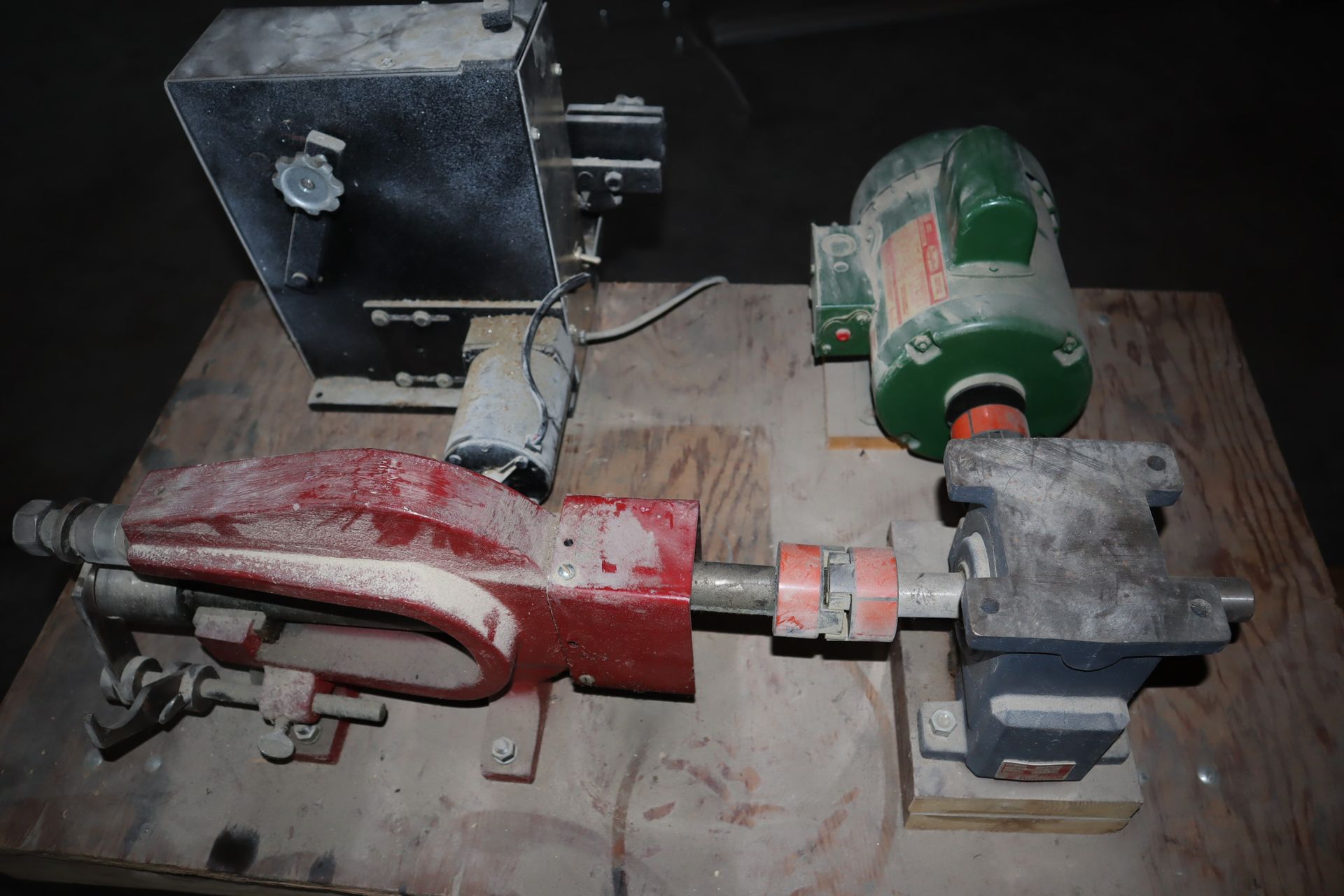 A dusty, industrial machine with a motor, connected to a pump-like red and gray assembly, on a wooden platform.