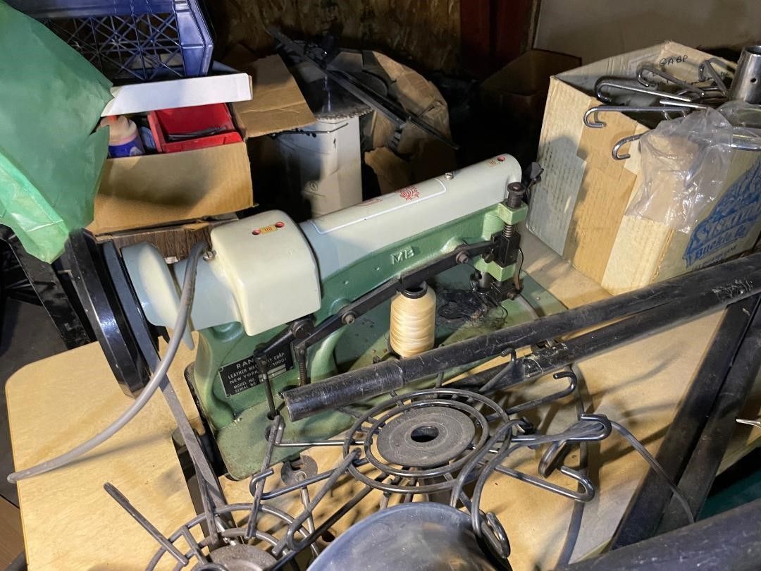Sewing machine on a cluttered surface with boxes, other mechanical parts, and a spool of thread.
