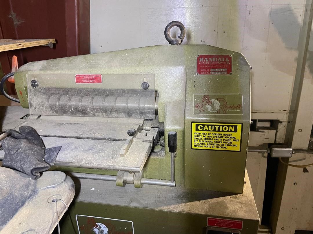 A dusty, green wood planer machine with red and yellow labels in a workshop.