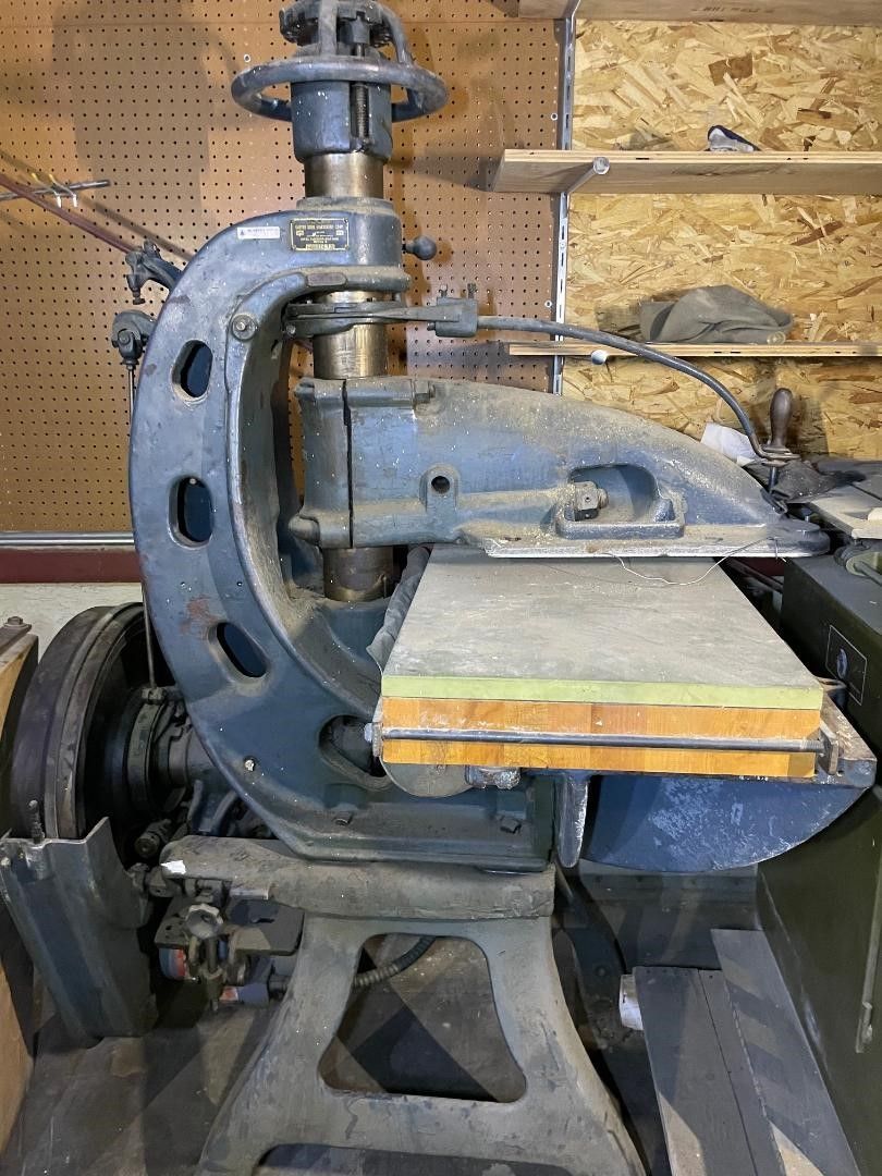 Old industrial machine, blue-grey, with a large C-shaped frame, table, and overhead mechanism.