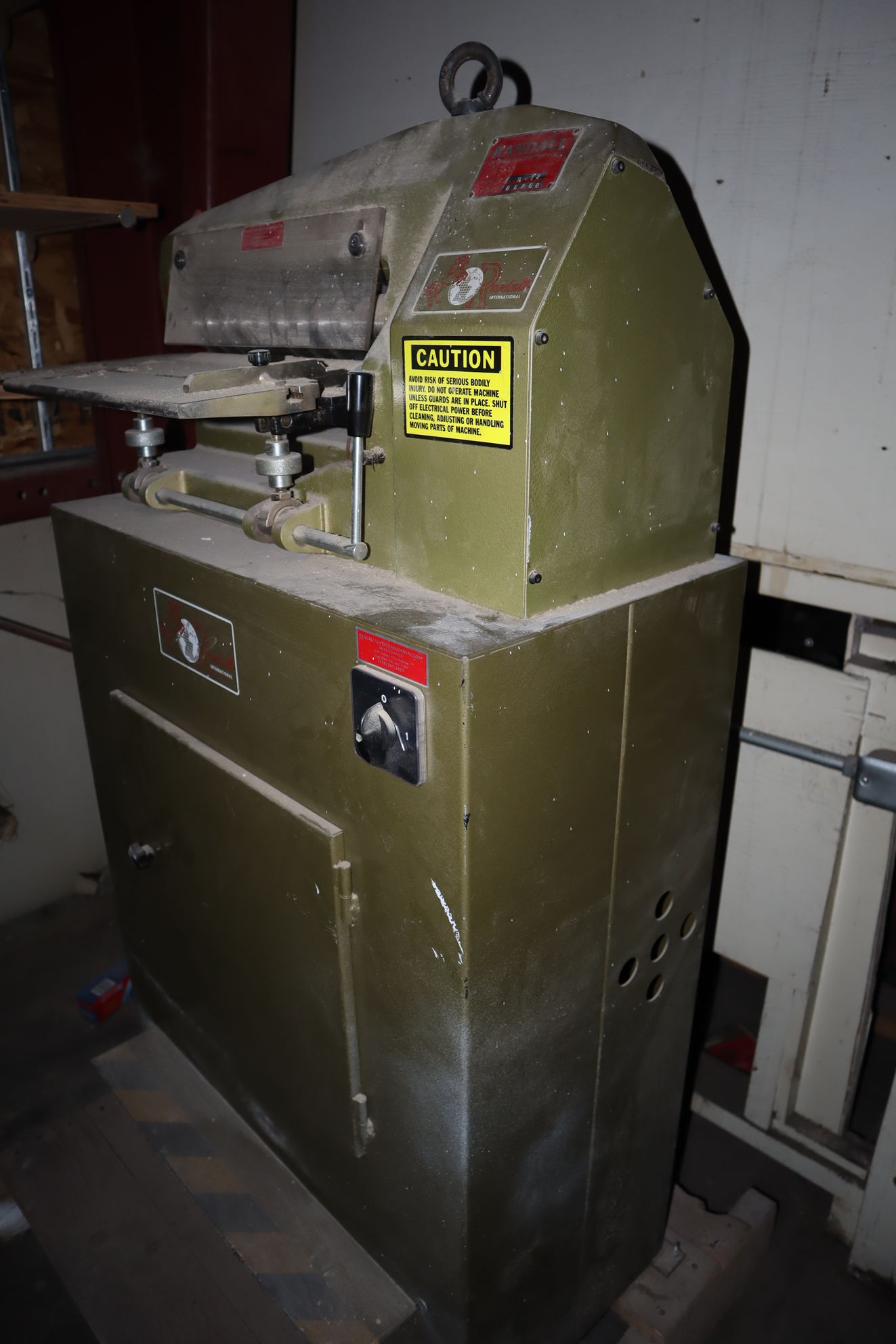 Old, olive-green industrial machine with a cutting blade, likely for a factory setting.