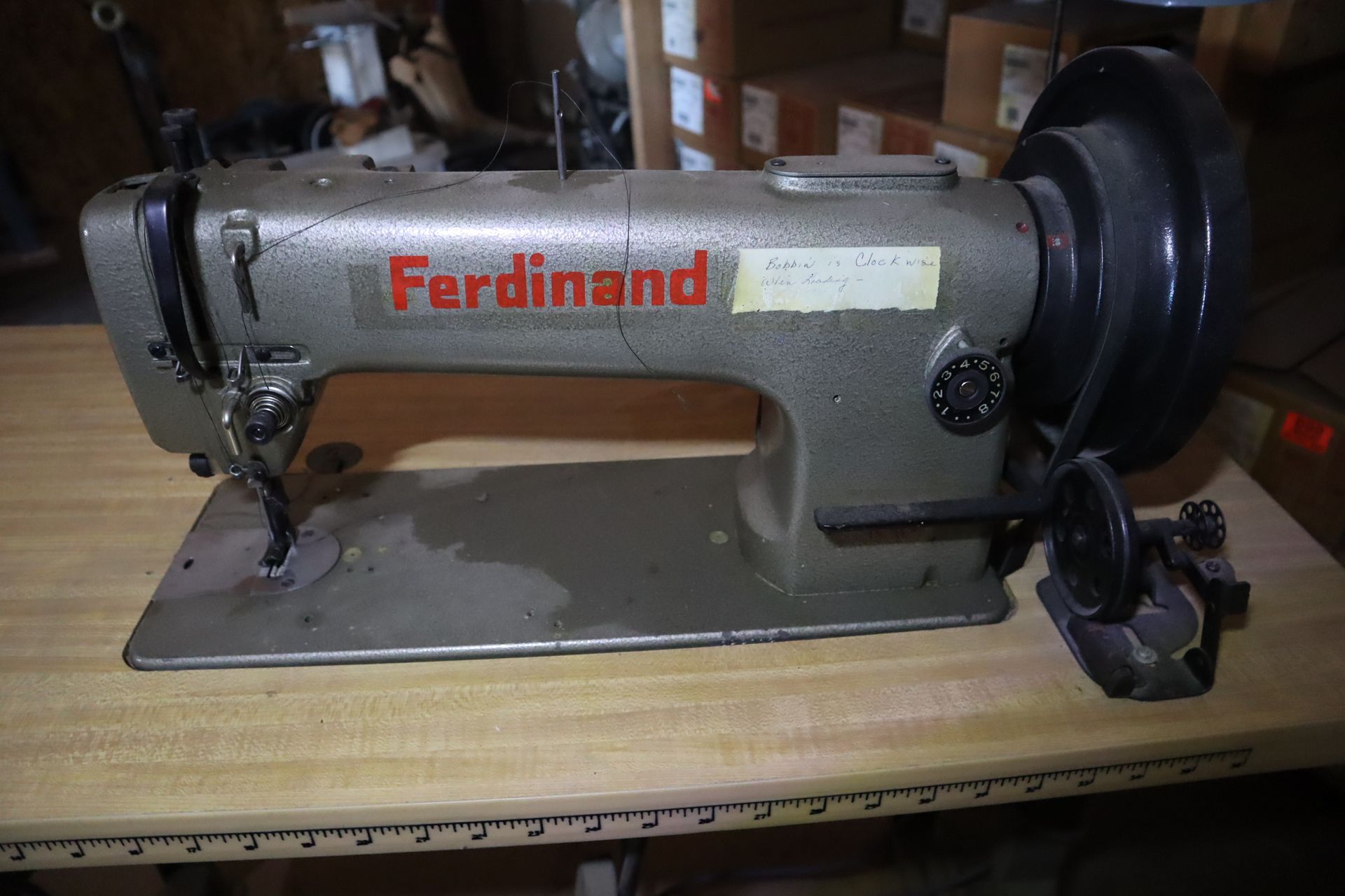 A grey Ferdinand industrial sewing machine with a red logo on a wood surface.