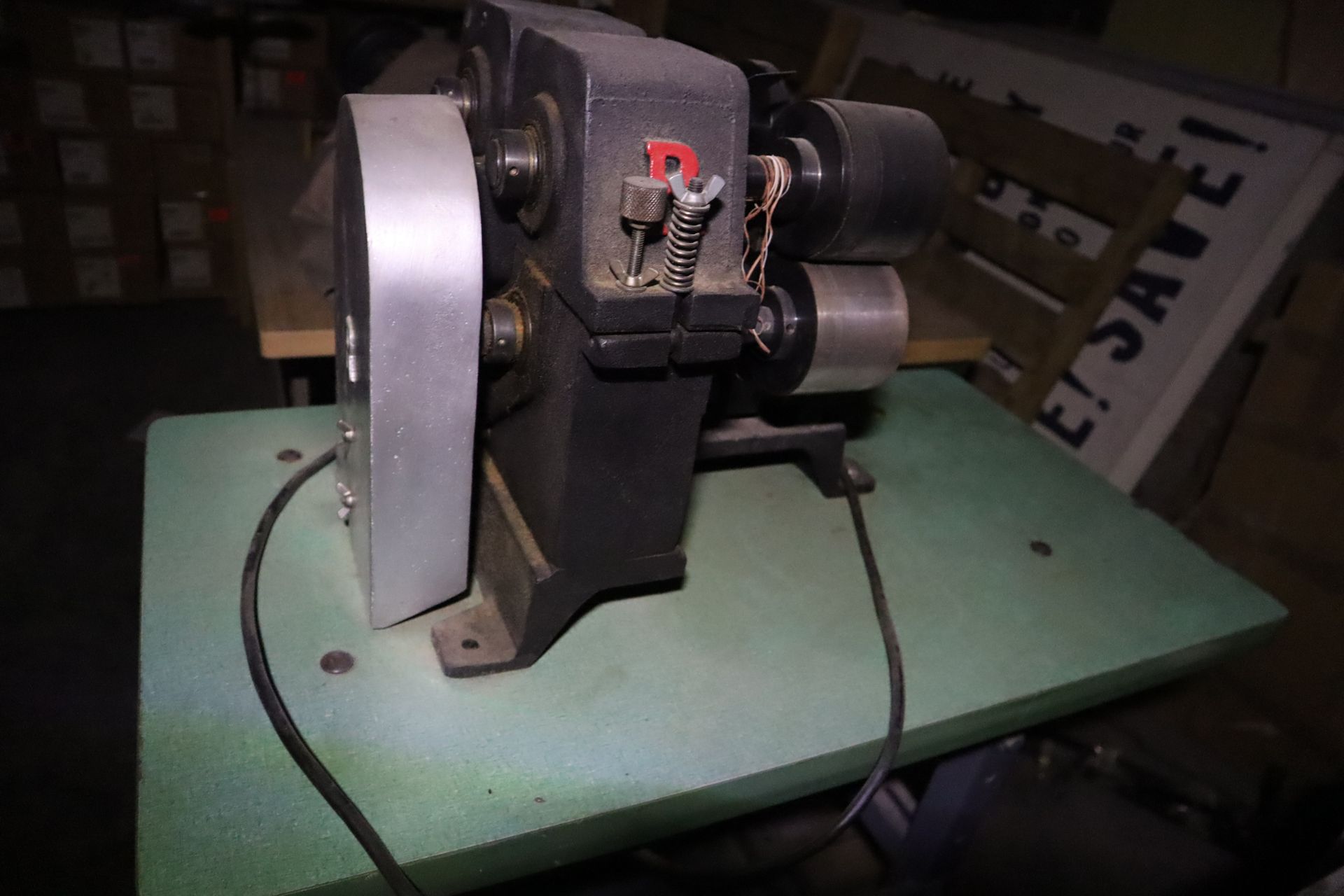 Black industrial machine on a green surface, with a large silver wheel and black power cord.