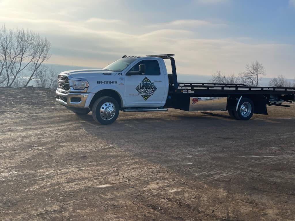 A white flatbed tow truck parked on a dirt lot under a bright sky.