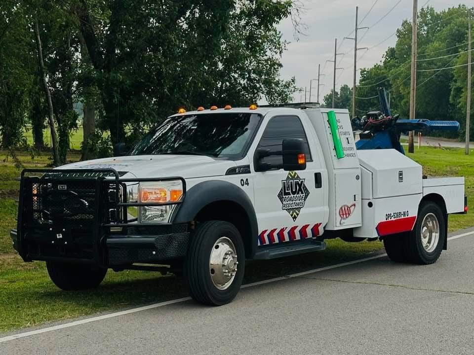 A white utility truck with LUX branding and a front brush guard parked on the side of a grassy road.
