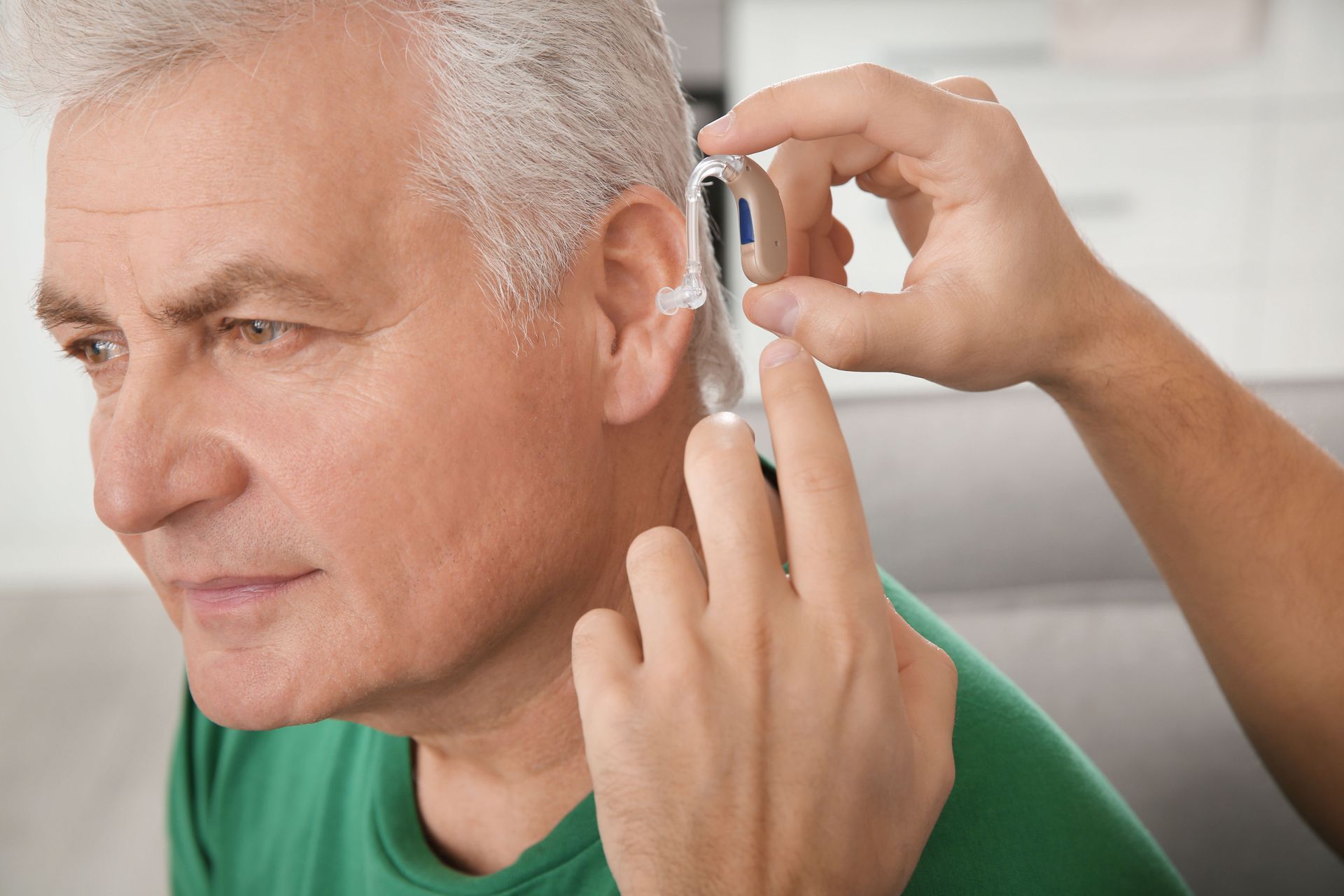 A person assists an individual in fitting a behind-the-ear hearing aid into their ear.
