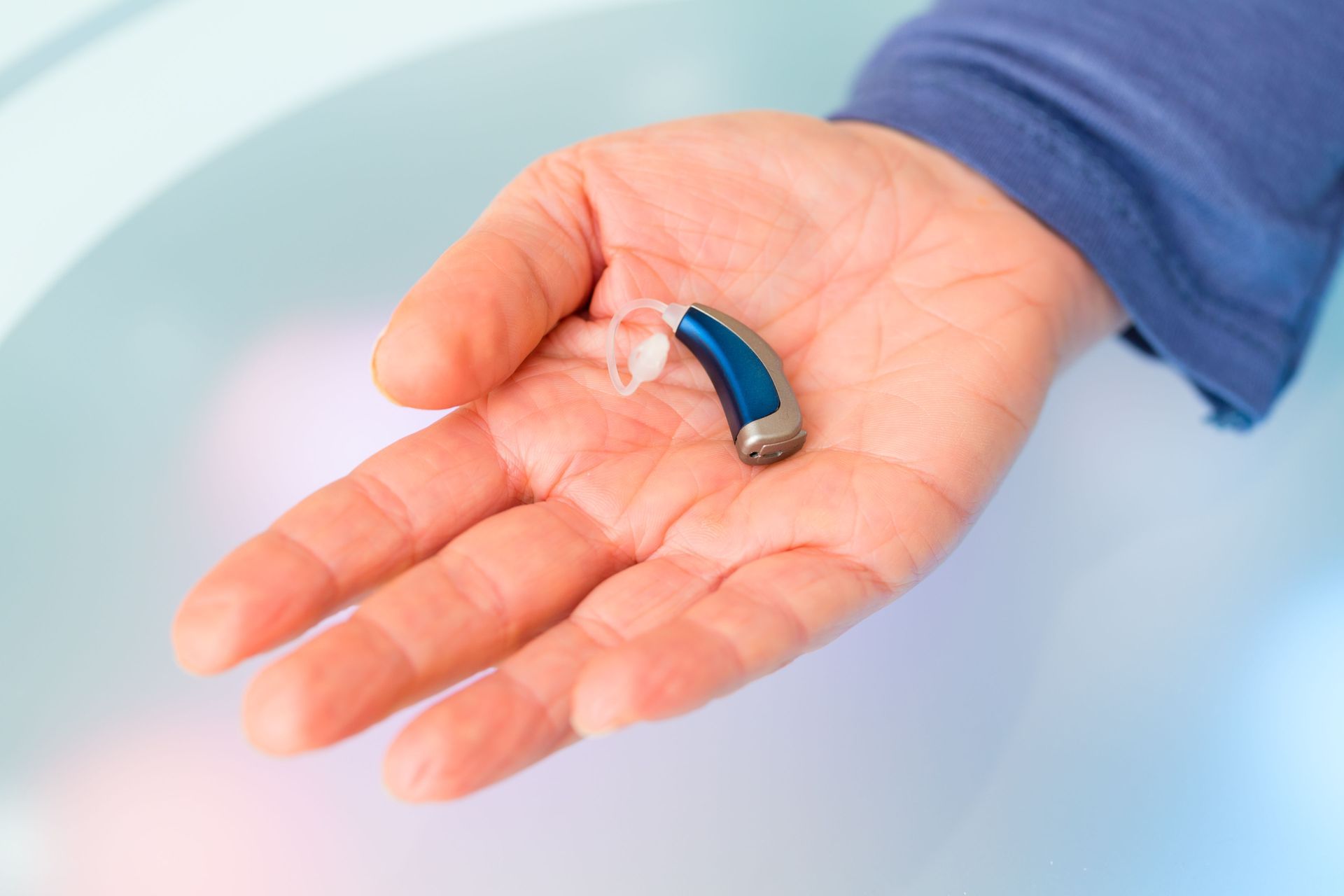 A blue, behind-the-ear hearing aid resting in the palm of a hand.