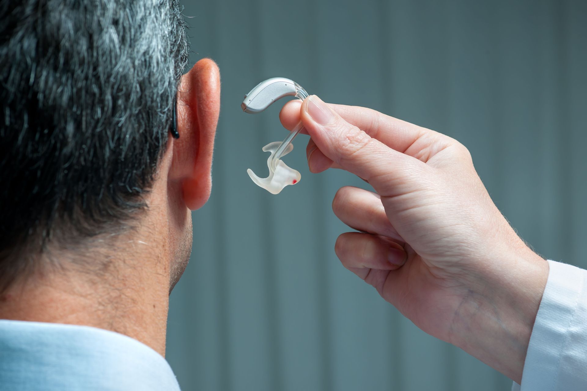 A professional holding a small behind-the-ear hearing aid near a person’s ear.