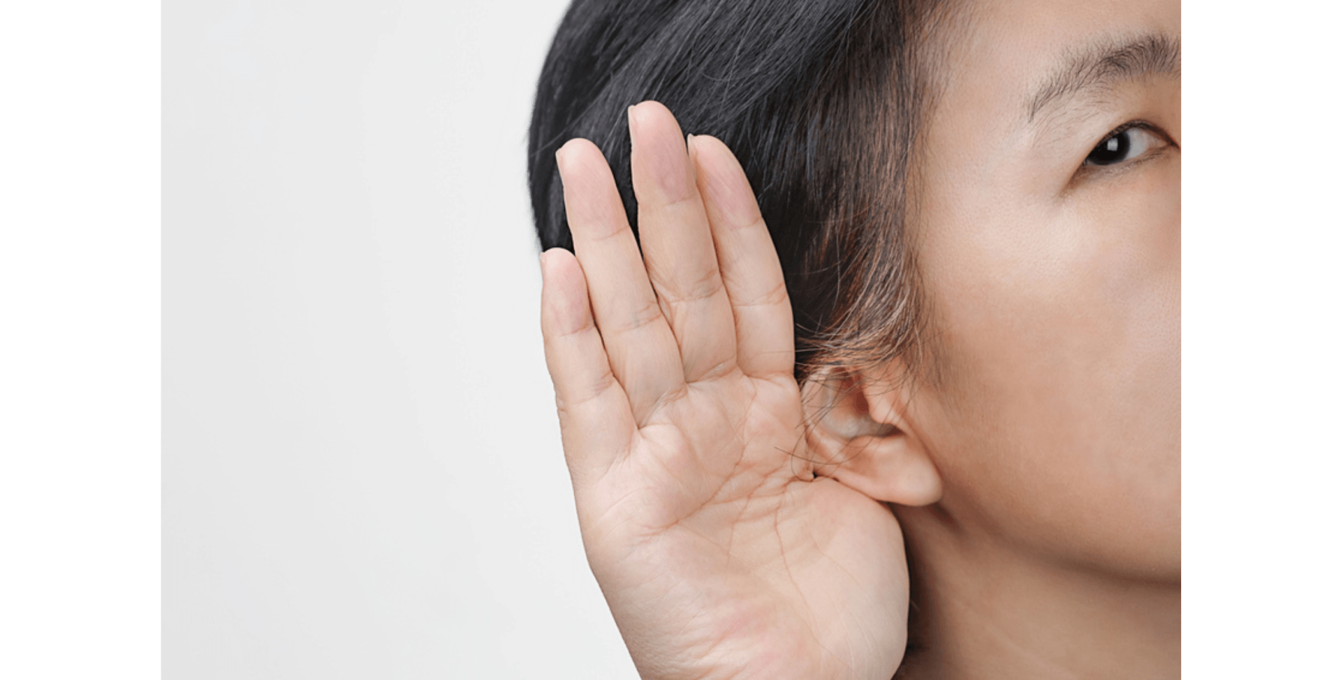 A person cupping their hand behind their ear to listen carefully, set against a neutral background.