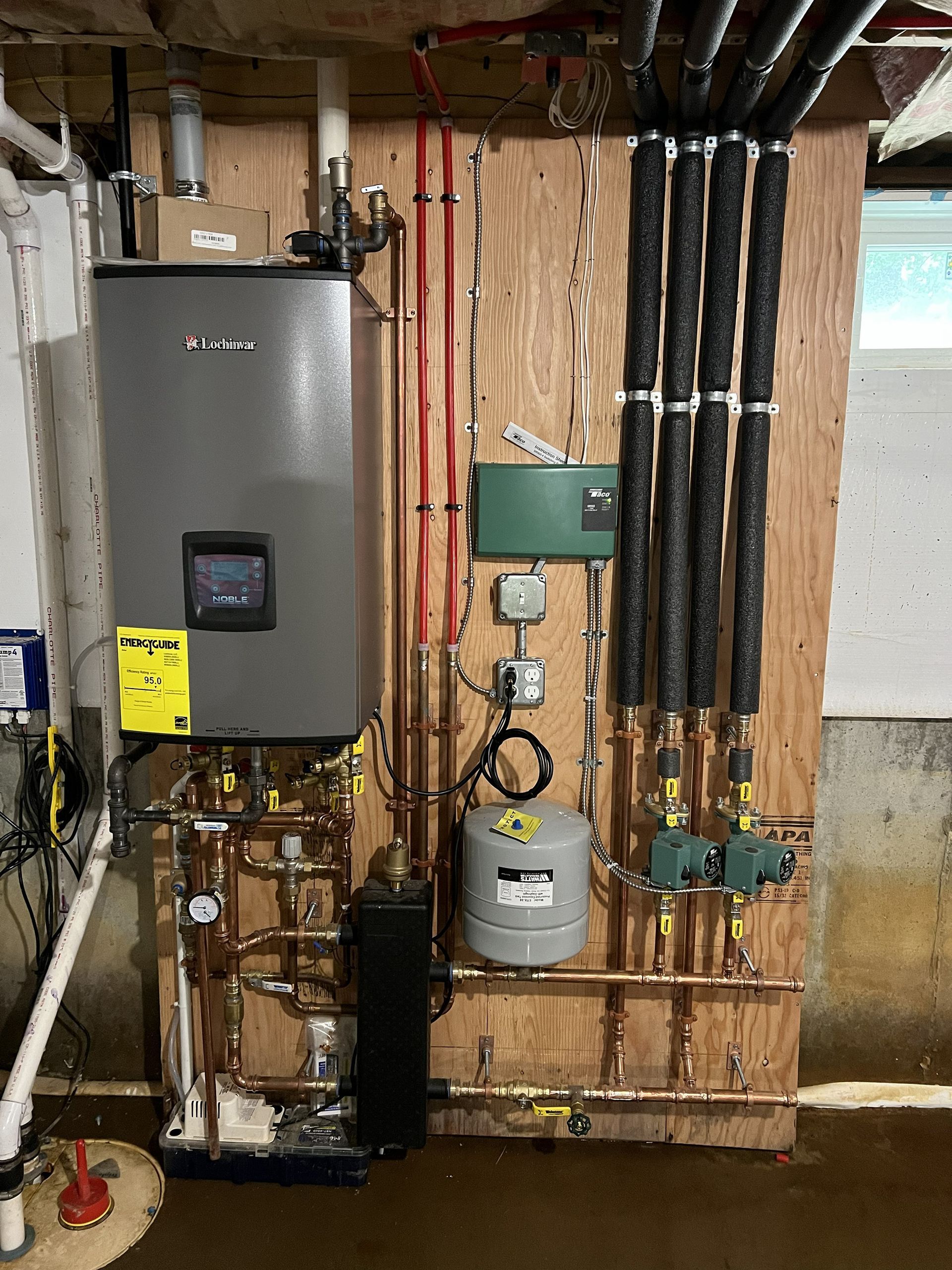 Residential utility room with water heater, furnace, pipes, and electrical panels against exposed wooden walls.