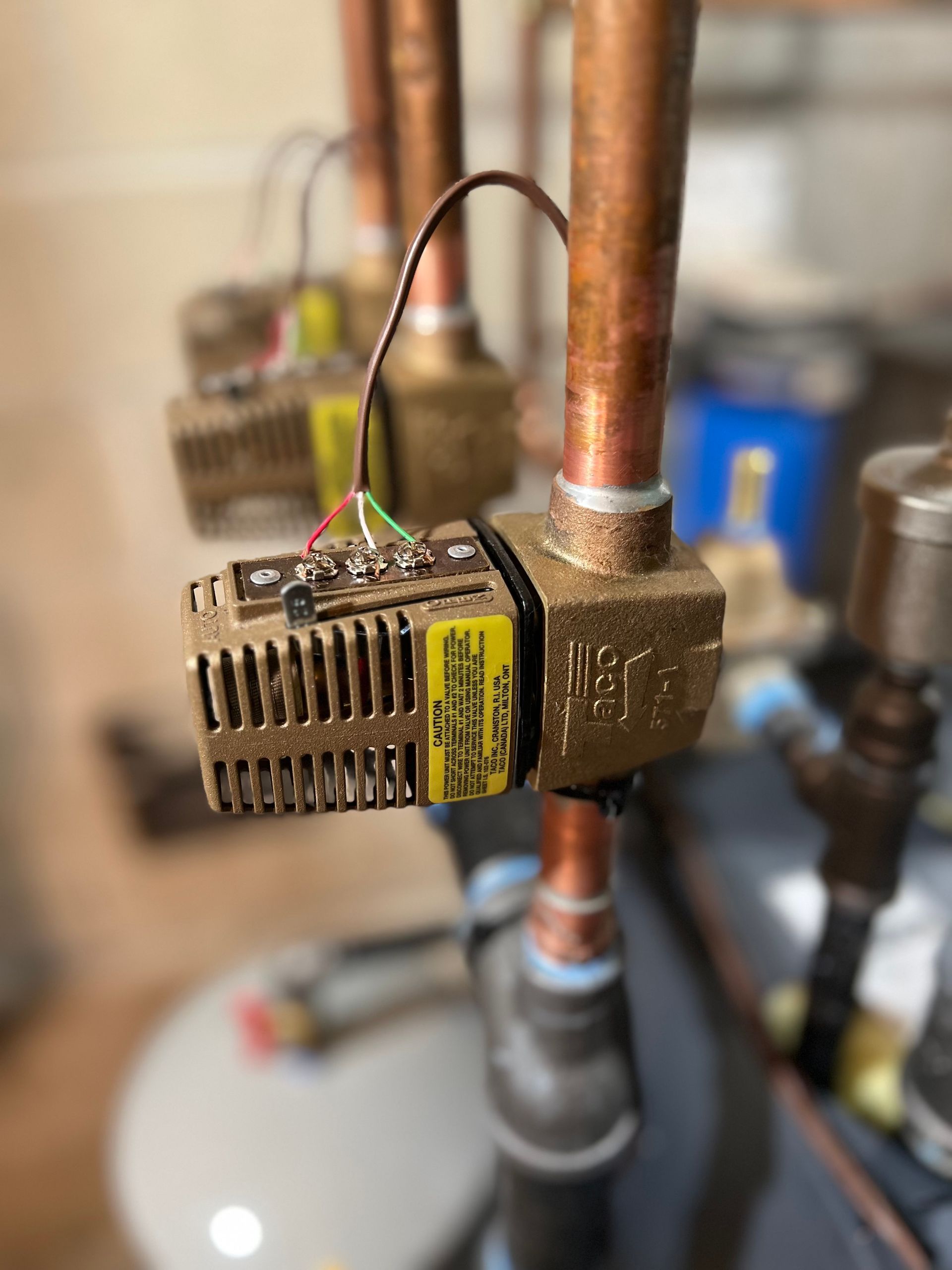 Small brass valve or sensor attached to a copper pipe with wires in a mechanical room