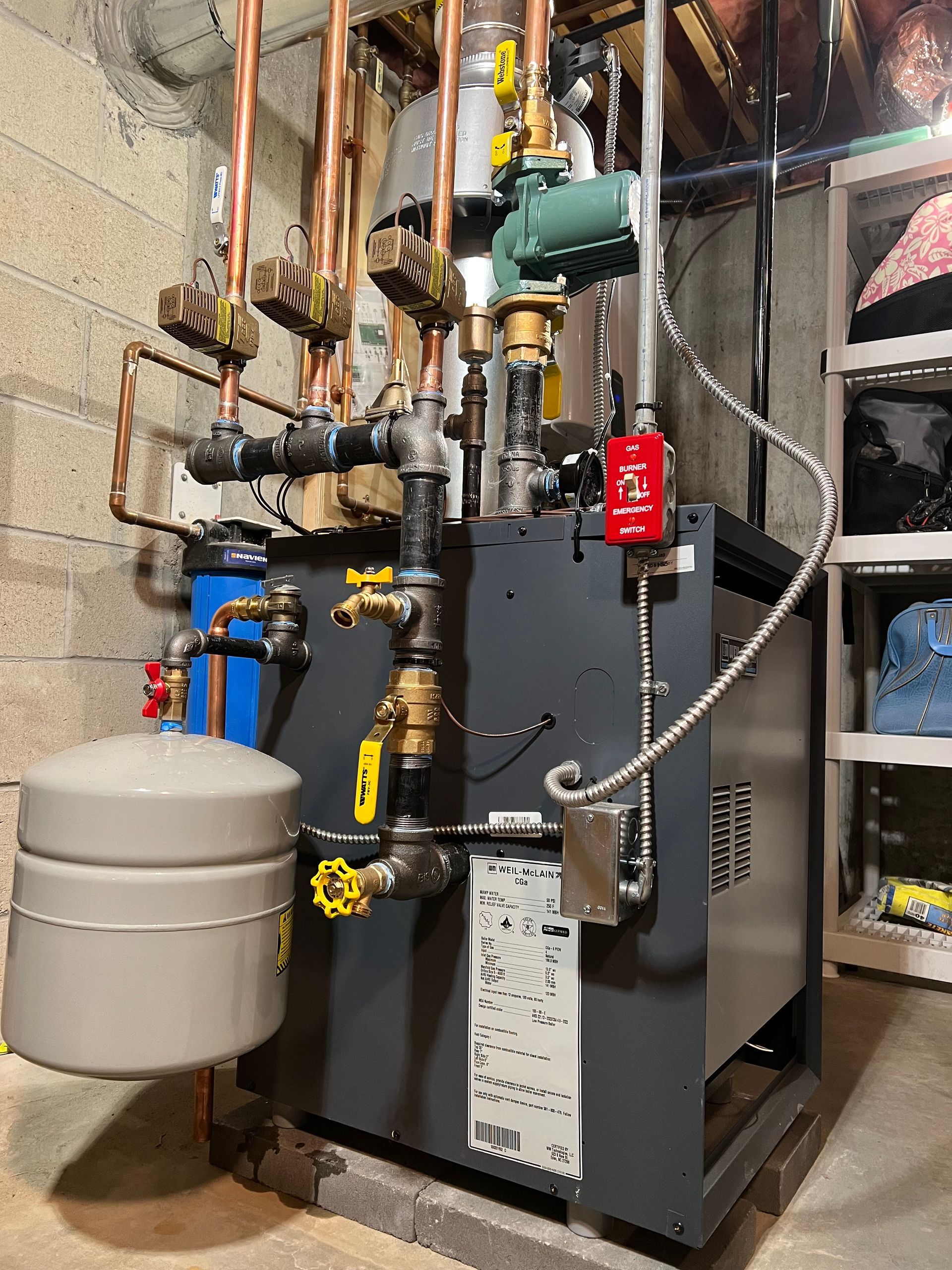 Industrial boiler with pipes, gauges, and a gray expansion tank in a utility room