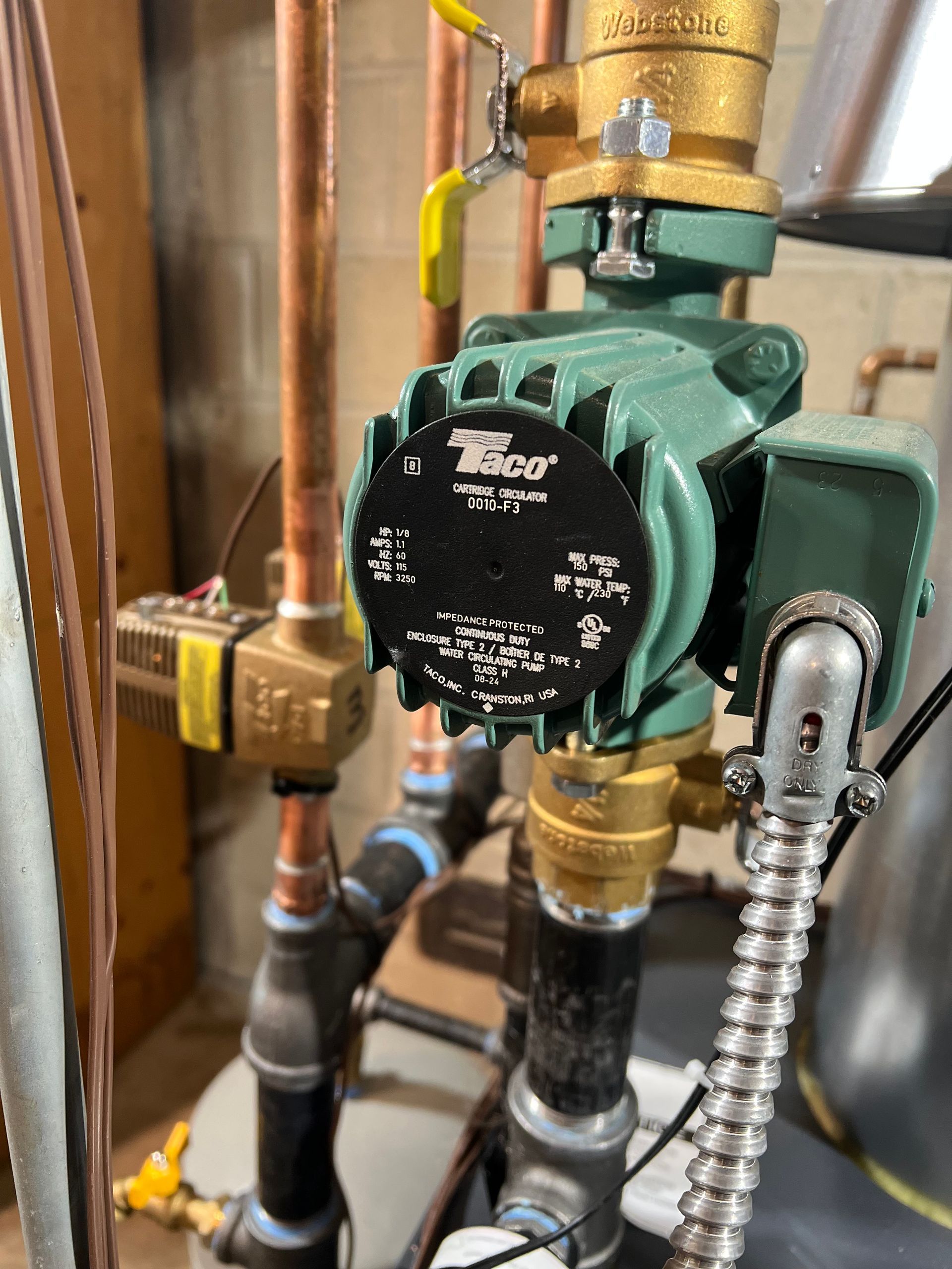 Green circulator pump with black control face on copper pipes in a utility room