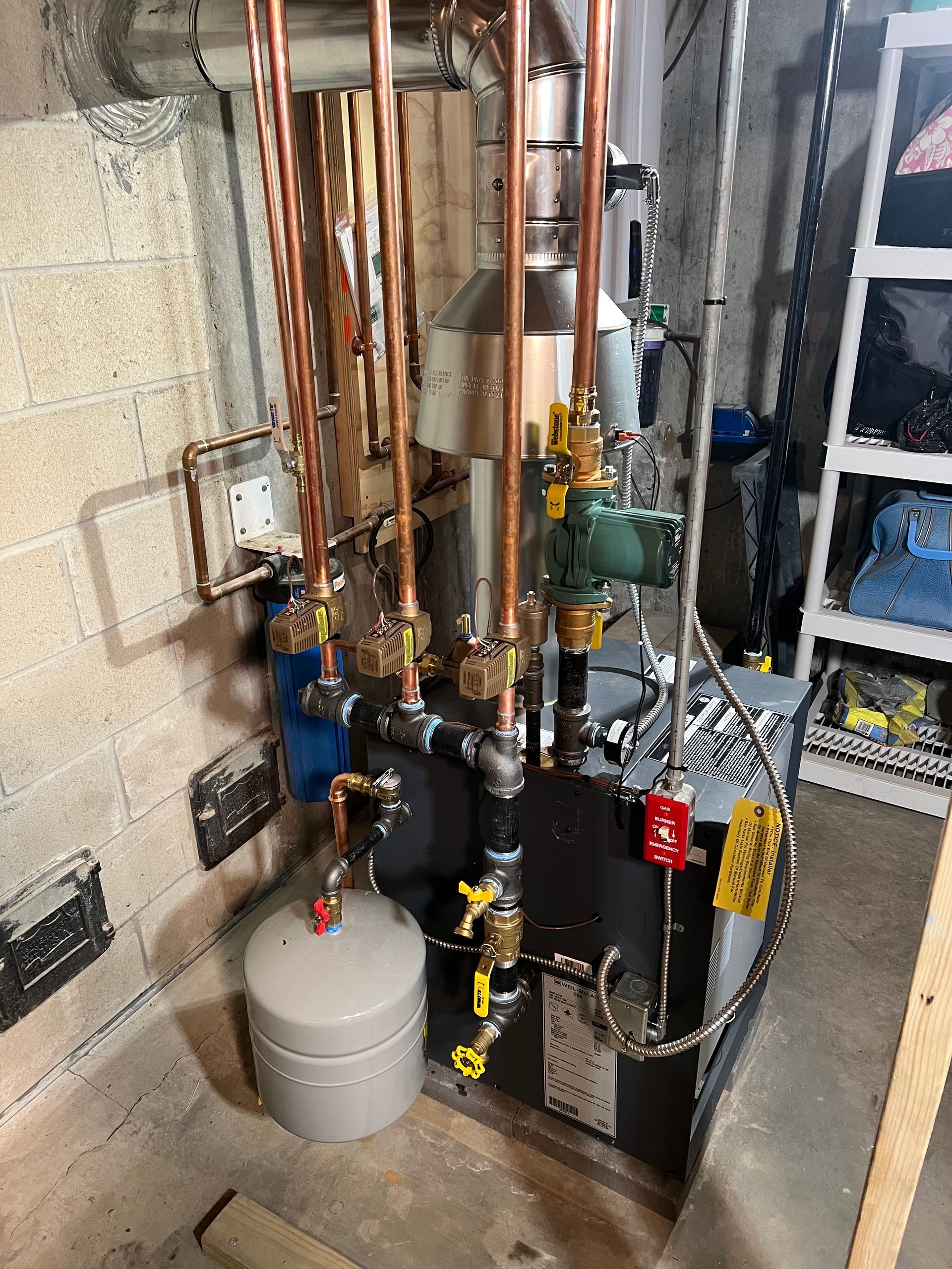 Compact basement boiler and plumbing system with copper pipes, gauges, valves, and a gray tank