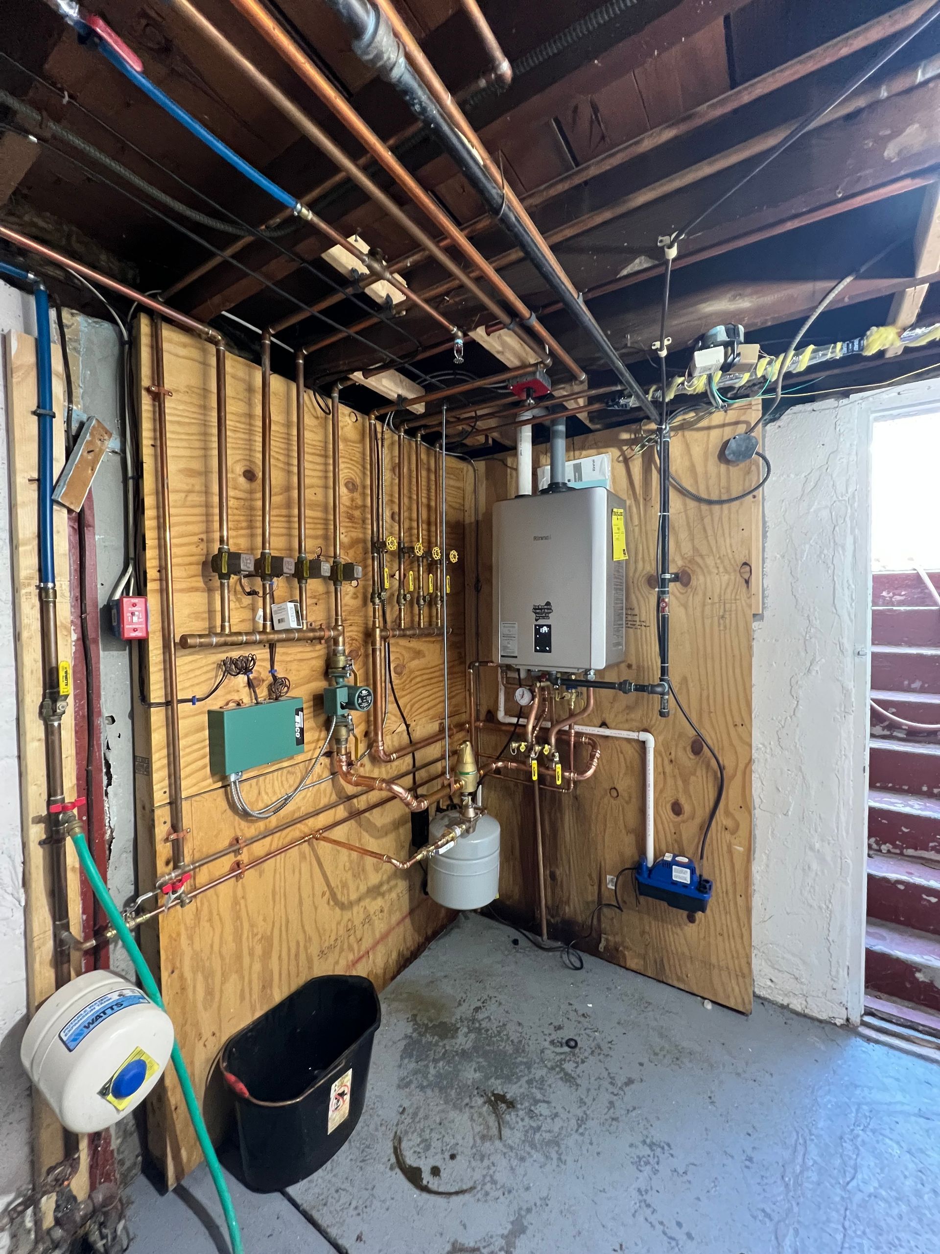 Partially renovated utility room with exposed wiring, pipes, water heater, and sink beside a doorway