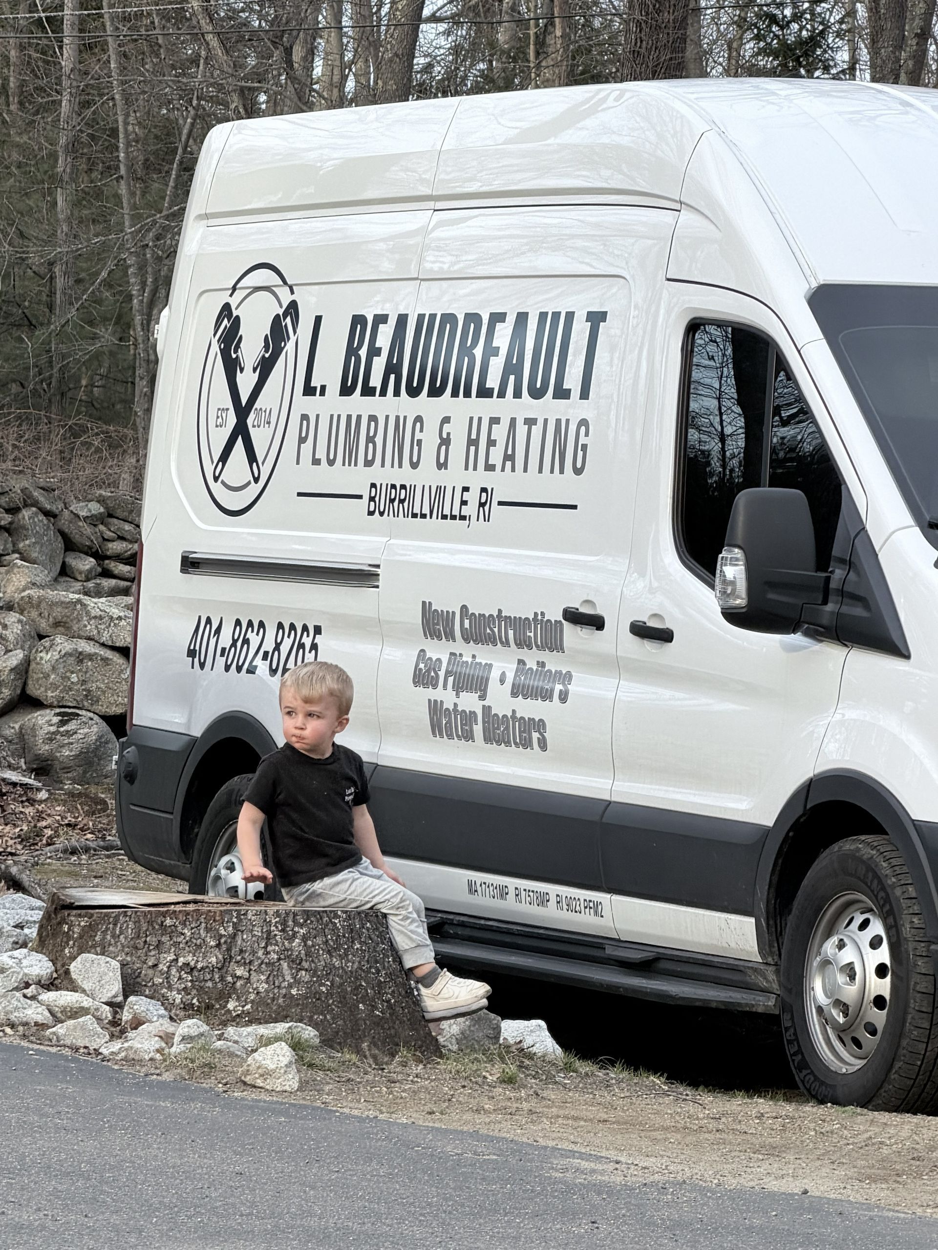 White service van with business logo parked by a stone wall; a child sits in front on a rocky roadside.