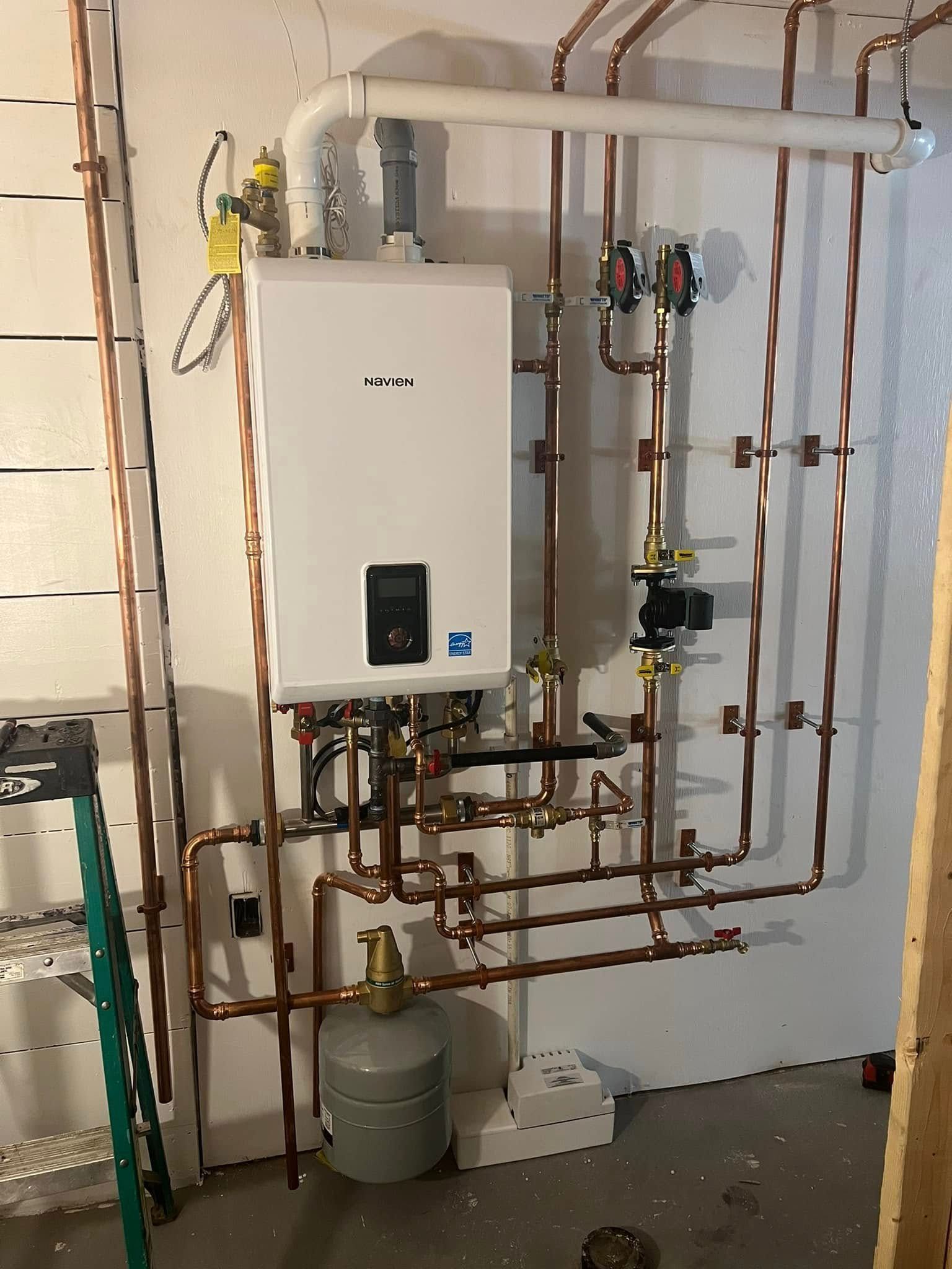 Wall-mounted boiler with extensive copper piping in a utility room, with a gray tank on the floor.