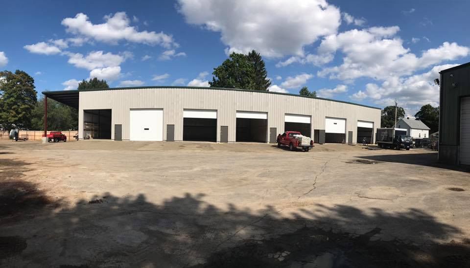 Wide white industrial building with garage doors and a red truck on a dirt lot under a clear sky