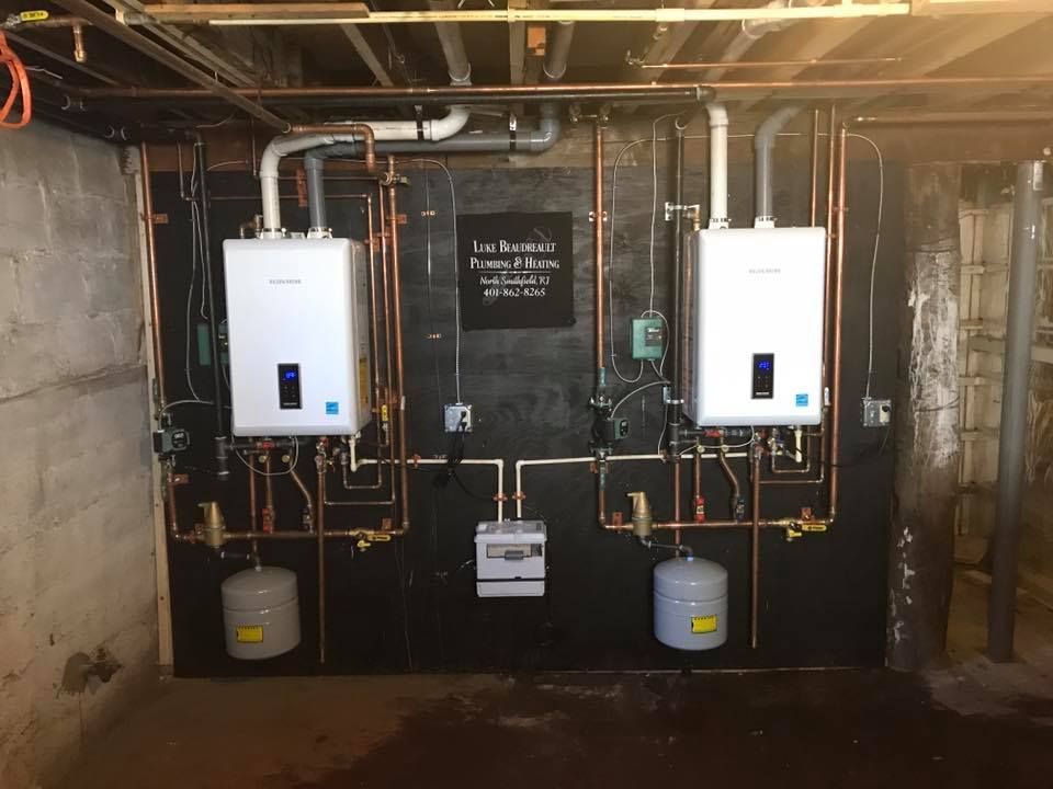 Basement utility room with two wall-mounted boilers, exposed pipes, and a black back wall.