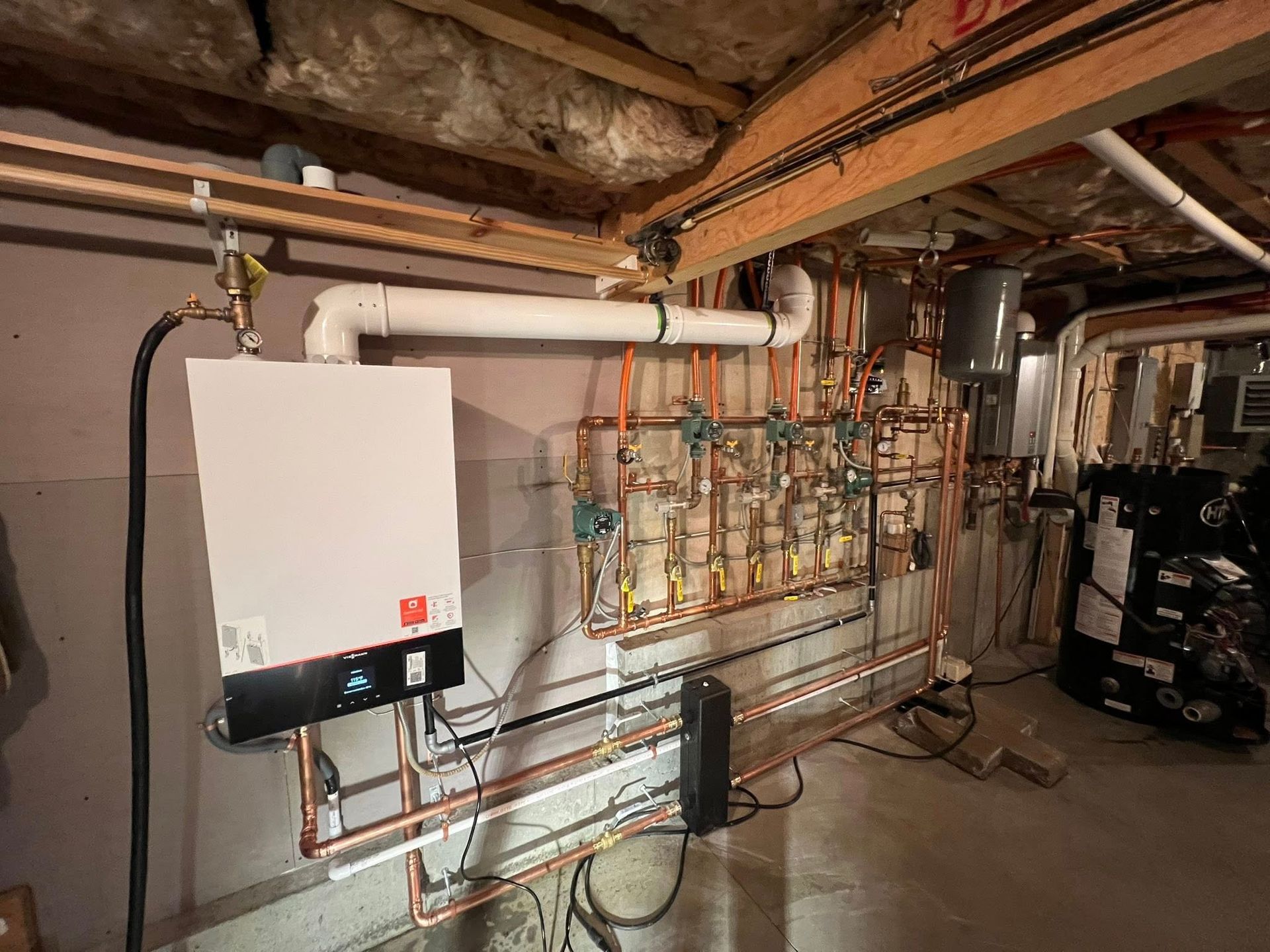 Basement utility room with wall-mounted boiler, exposed pipes, and ceiling beams.