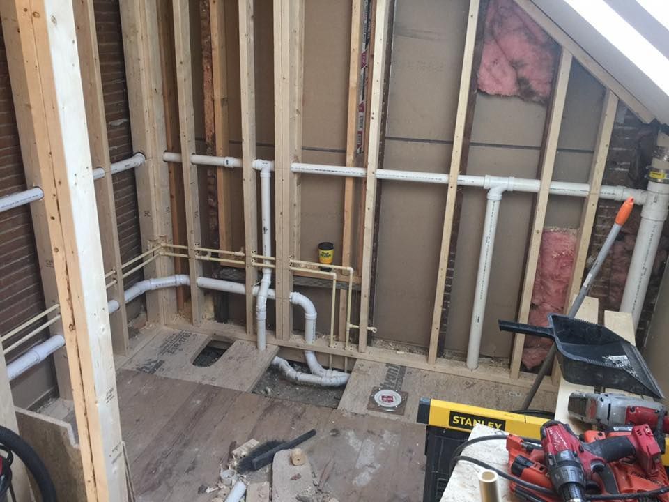 Unfinished bathroom framing with exposed studs, plumbing, insulation, and tools on the floor.
