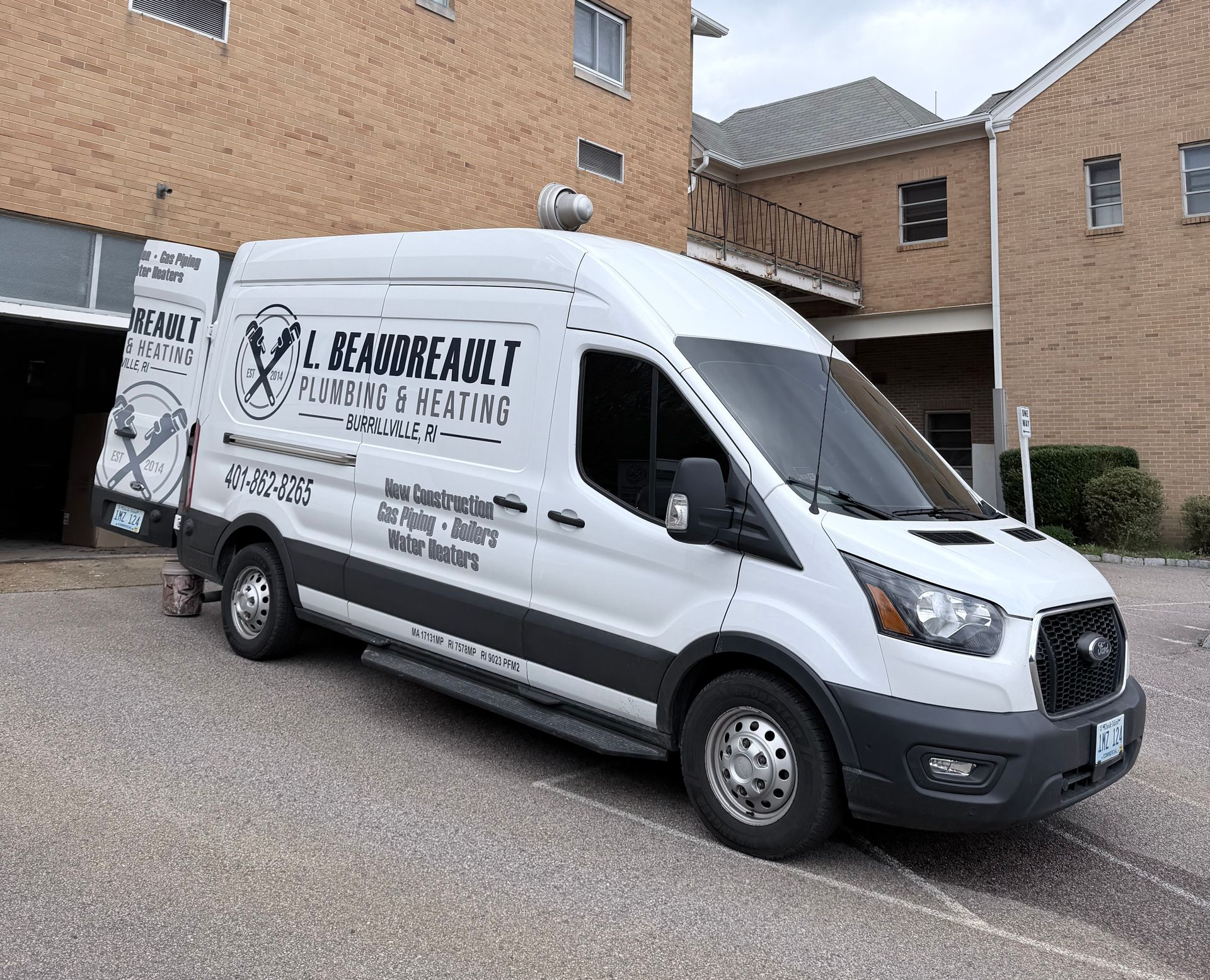 White service van parked beside brick apartment buildings on a gravel lot.