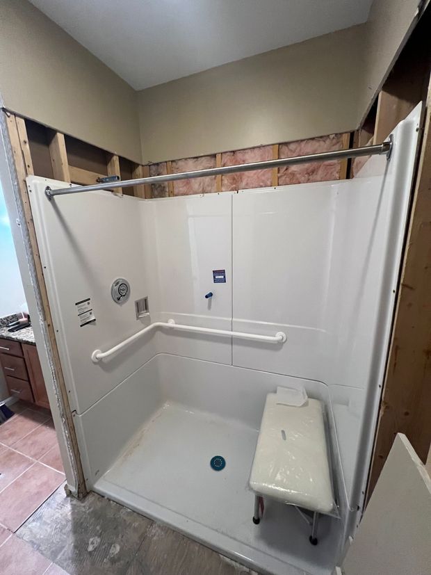 Accessible shower stall with white walls, grab bars, fold-down seat, and handheld showerhead in a bathroom
