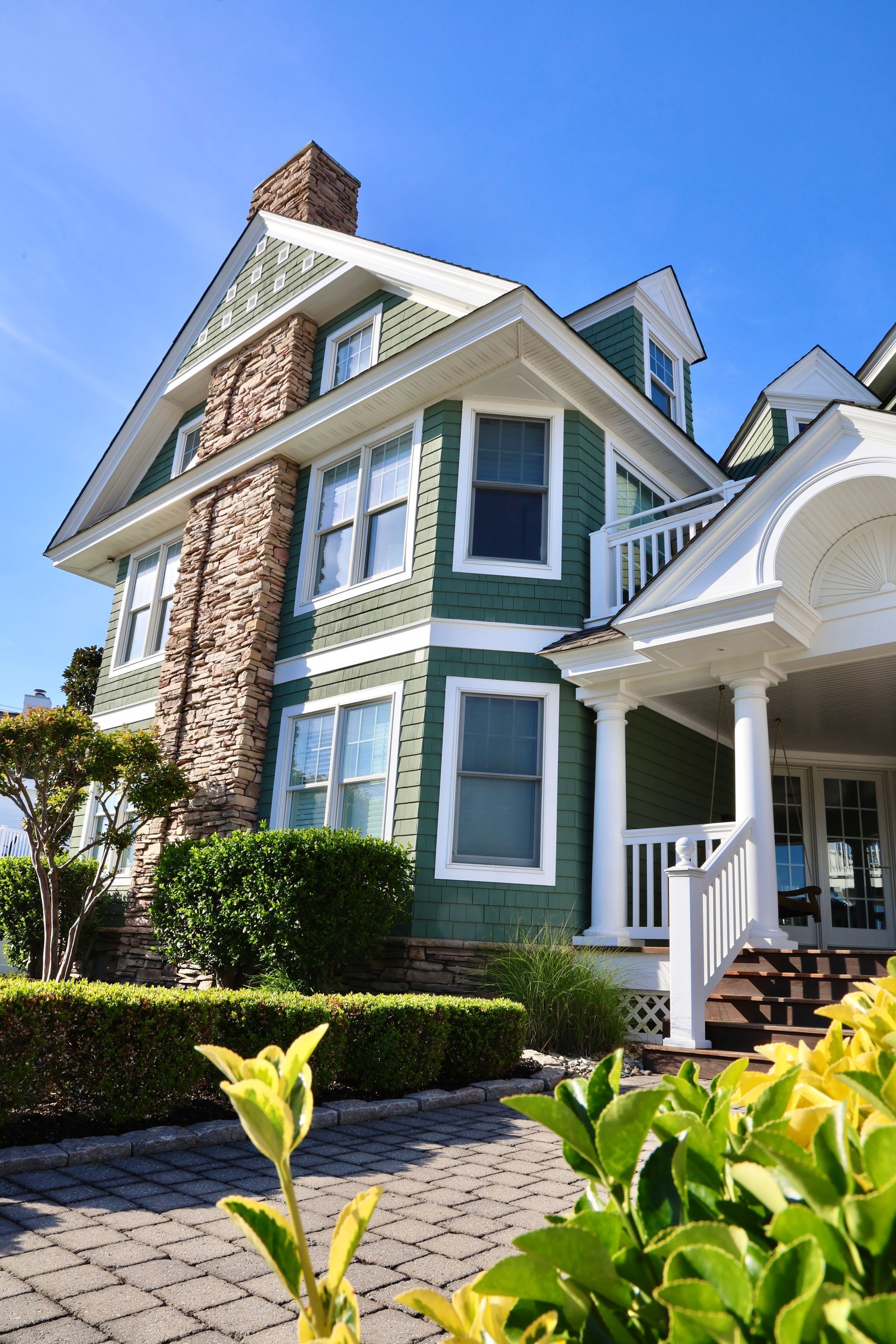 A large green house with a white porch and stairs