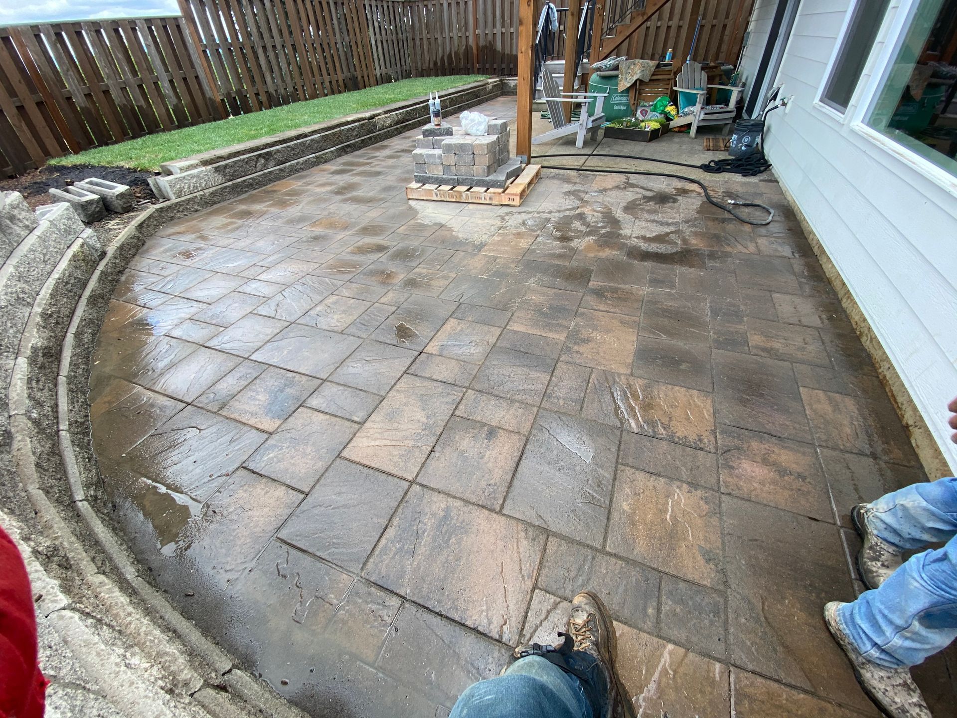 Patio under construction with gray pavers, curved edging, and tools near a house wall