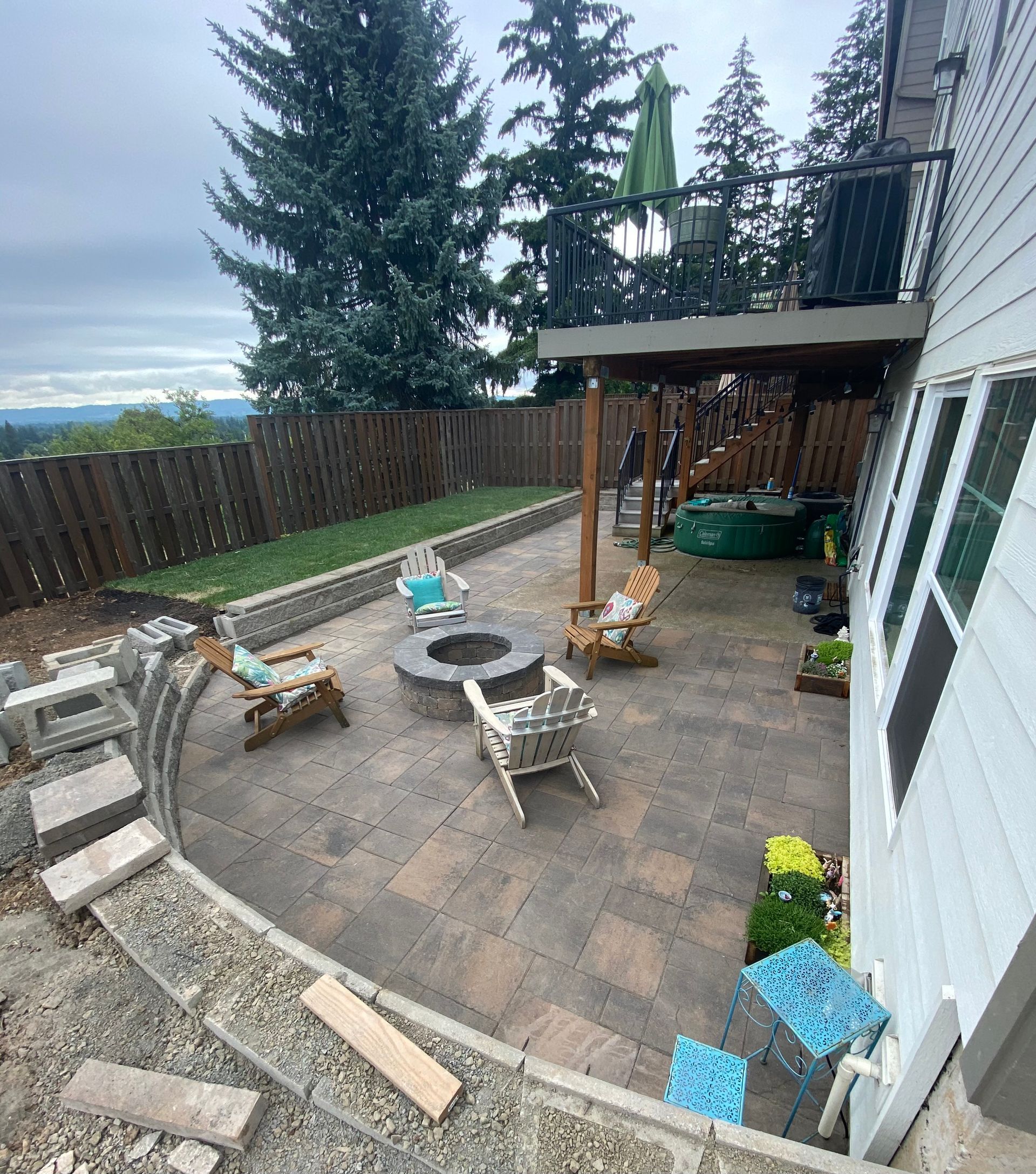 Back patio with patio furniture, pergola, potted plants, and tall evergreens beyond the fence.