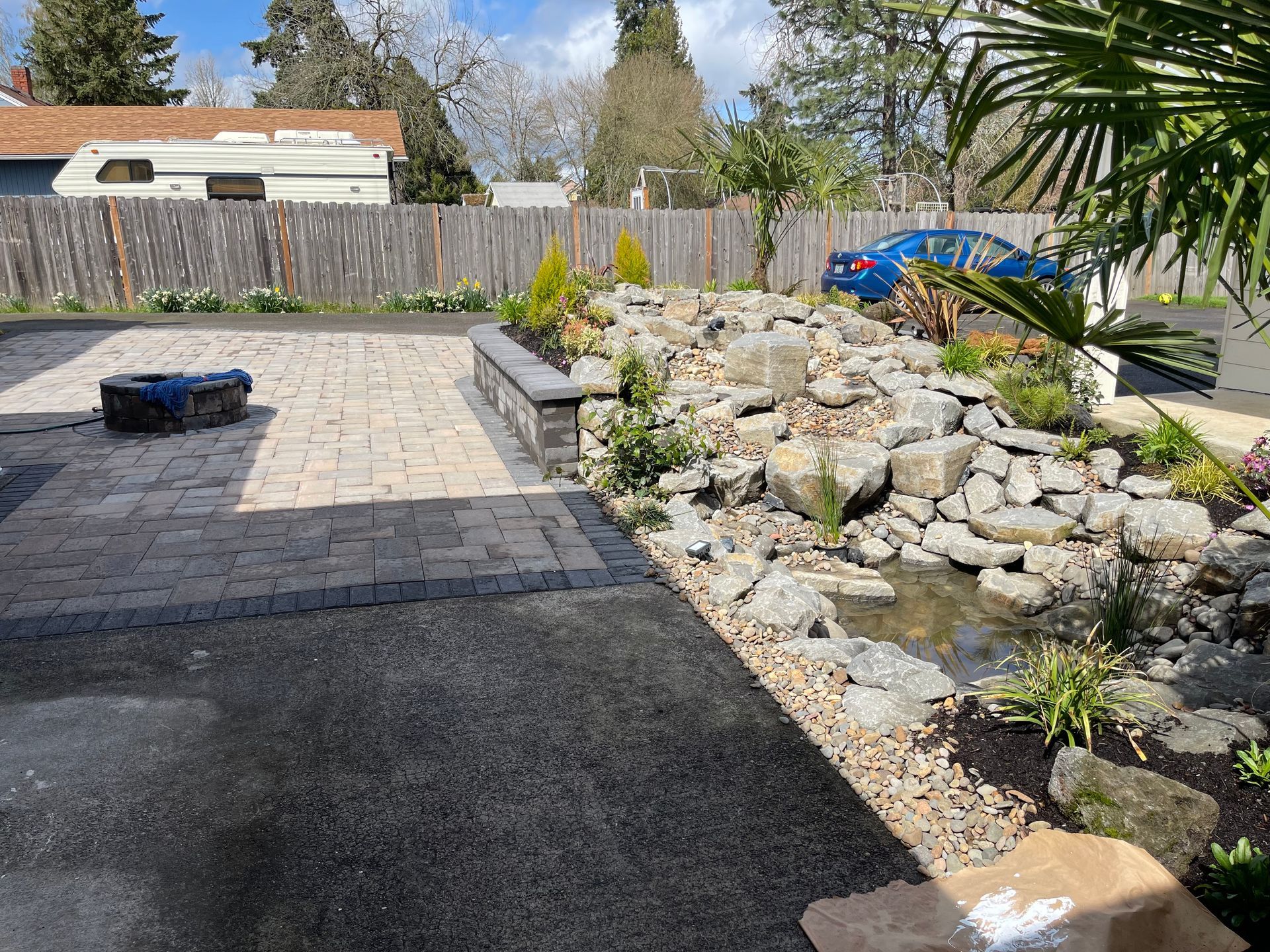 Backyard patio with stone path, rock garden, fence, and a blue wheelbarrow
