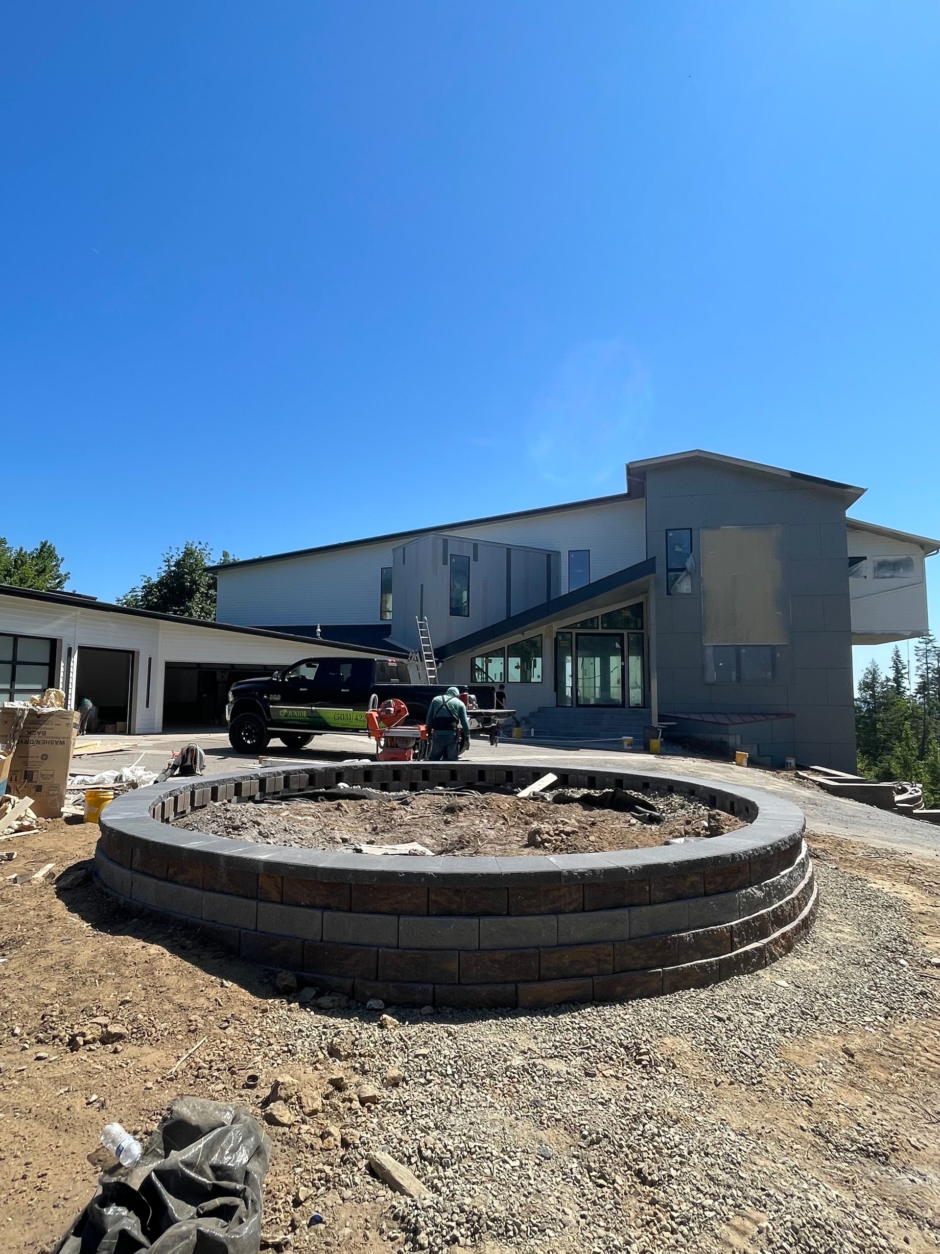 Modern house exterior with gravel yard and circular stone fire pit under a clear blue sky