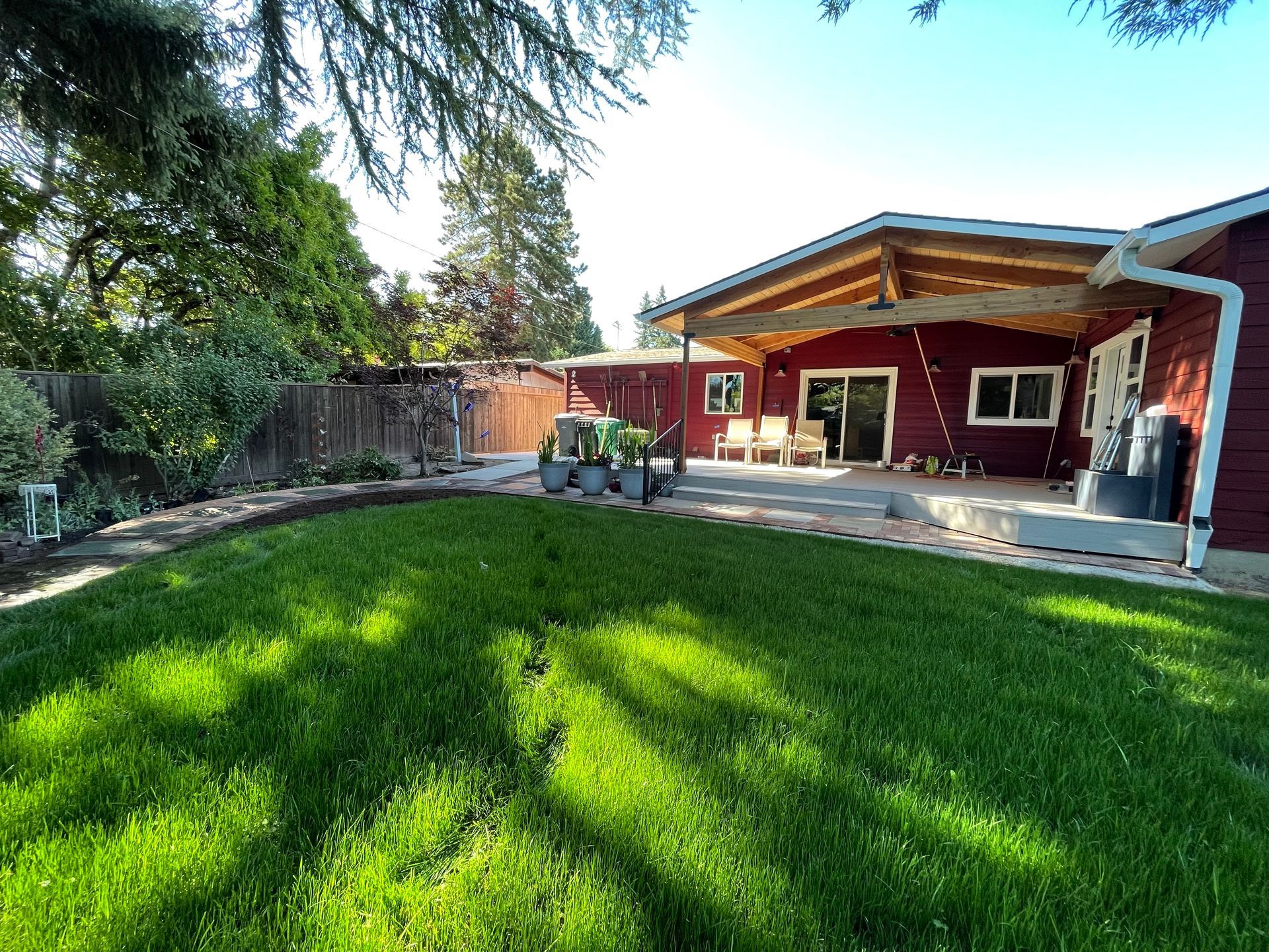 Backyard with green lawn, patio, red house, and a child on a toy vehicle near the deck